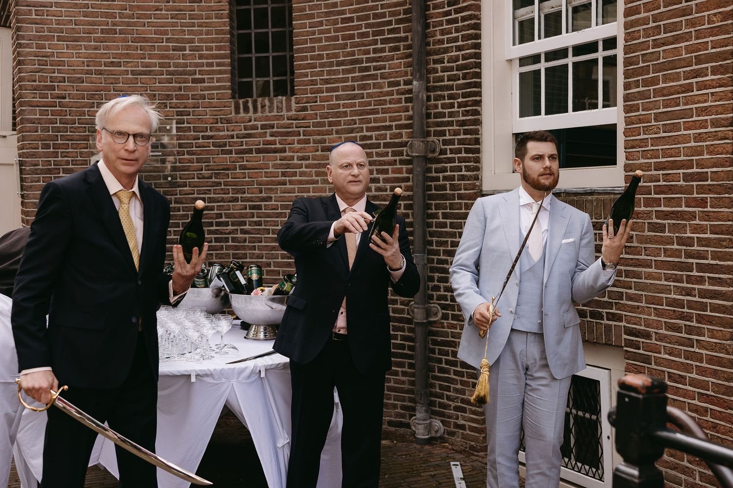 Wedding guests in formal attire standing outside brick building taking photos.