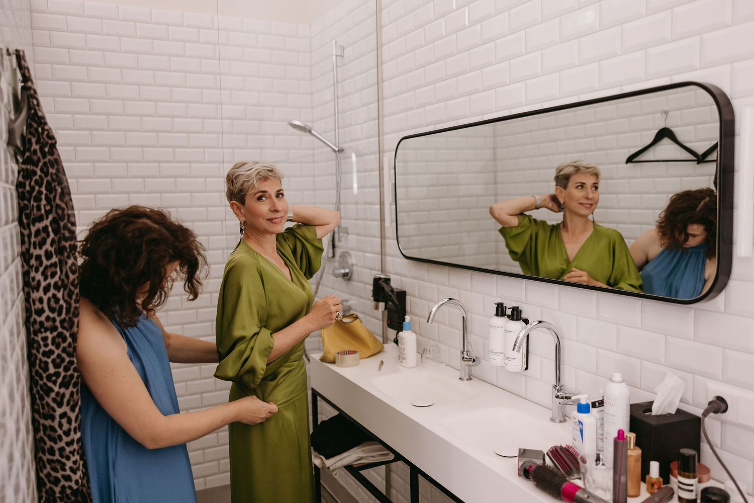 Interior of a bright white tiled bathroom with mirrors and personal care items.