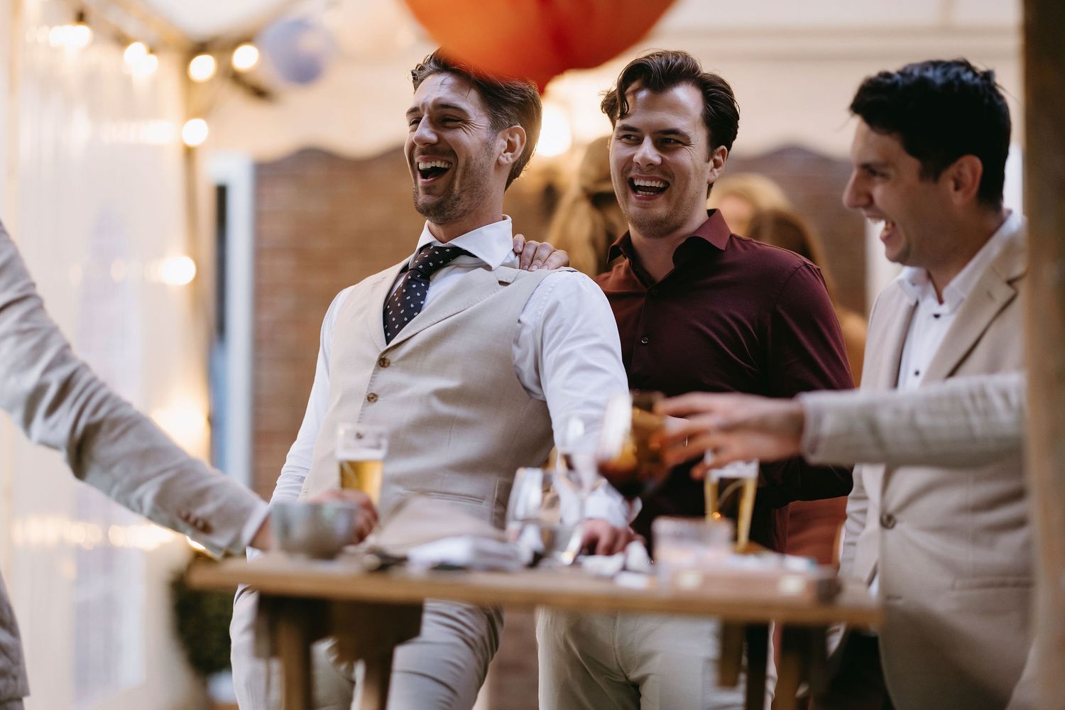 Wedding reception guests celebrating and toasting at tables with festive lighting.