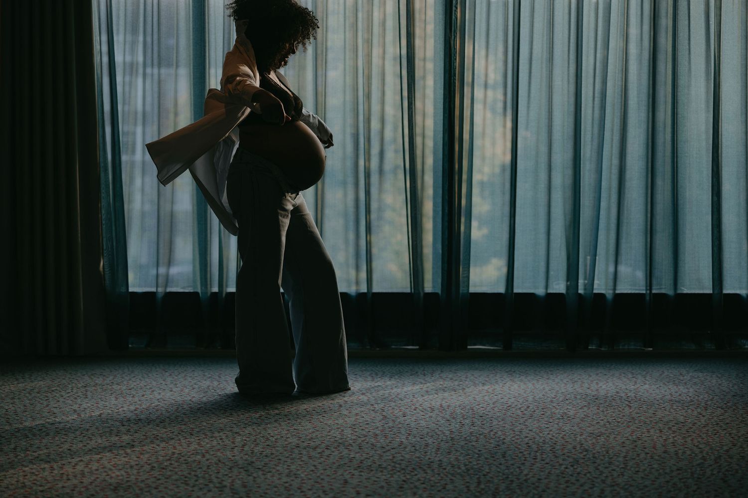 Silhouette against blue curtains in moody indoor lighting.