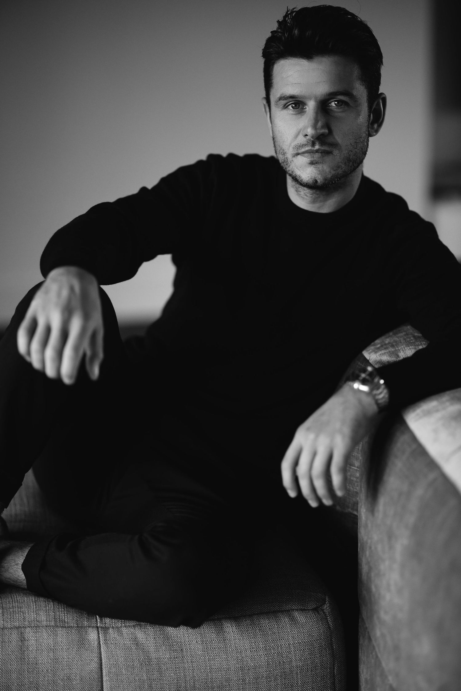 Dramatic black and white portrait series focusing on casual pose against textured background.