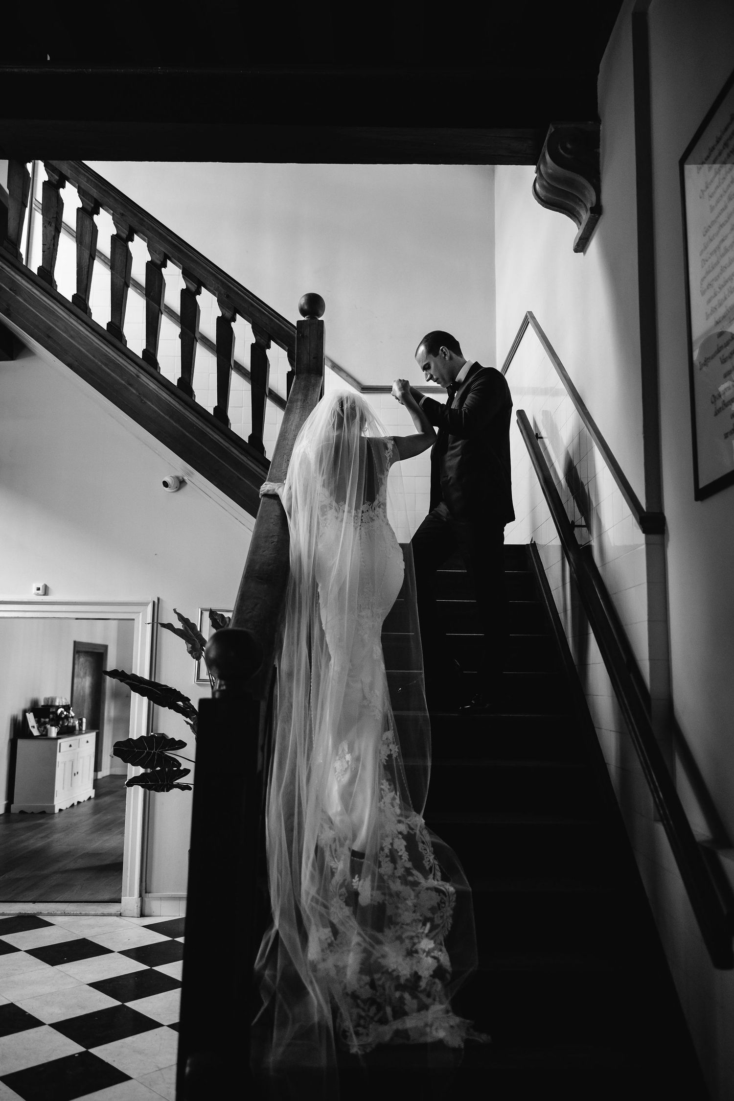 A black and white wedding photo of a couple ascending a staircase with a flowing veil trailing behind them.