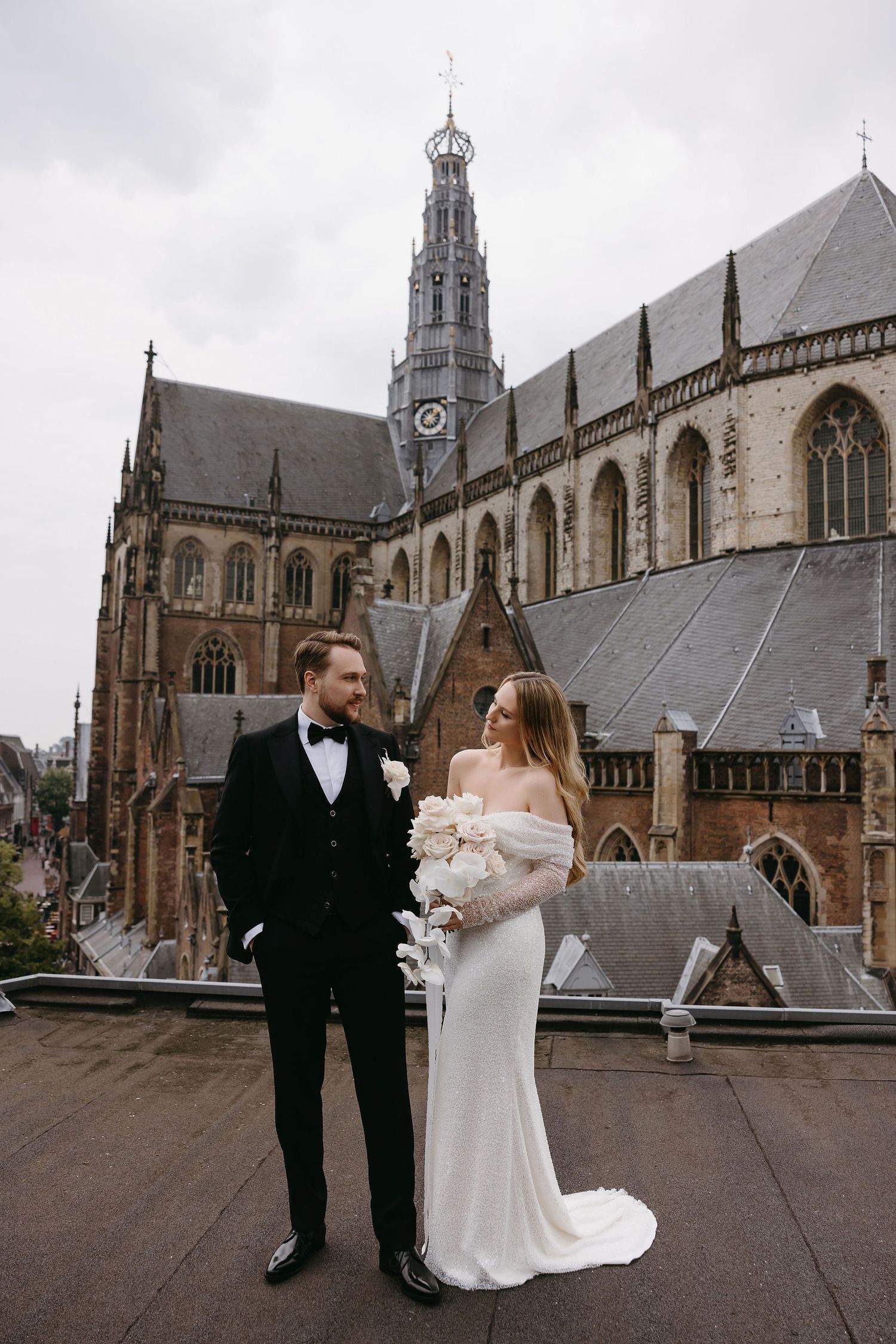 A newlywed couple poses in front of a grand Gothic cathedral with ornate spires and architecture on their wedding day.