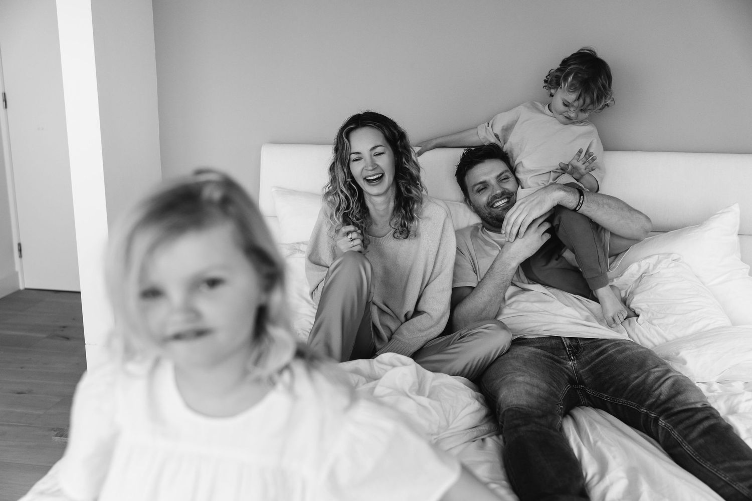 A playful family moment captured in black and white as they relax together on a bed.