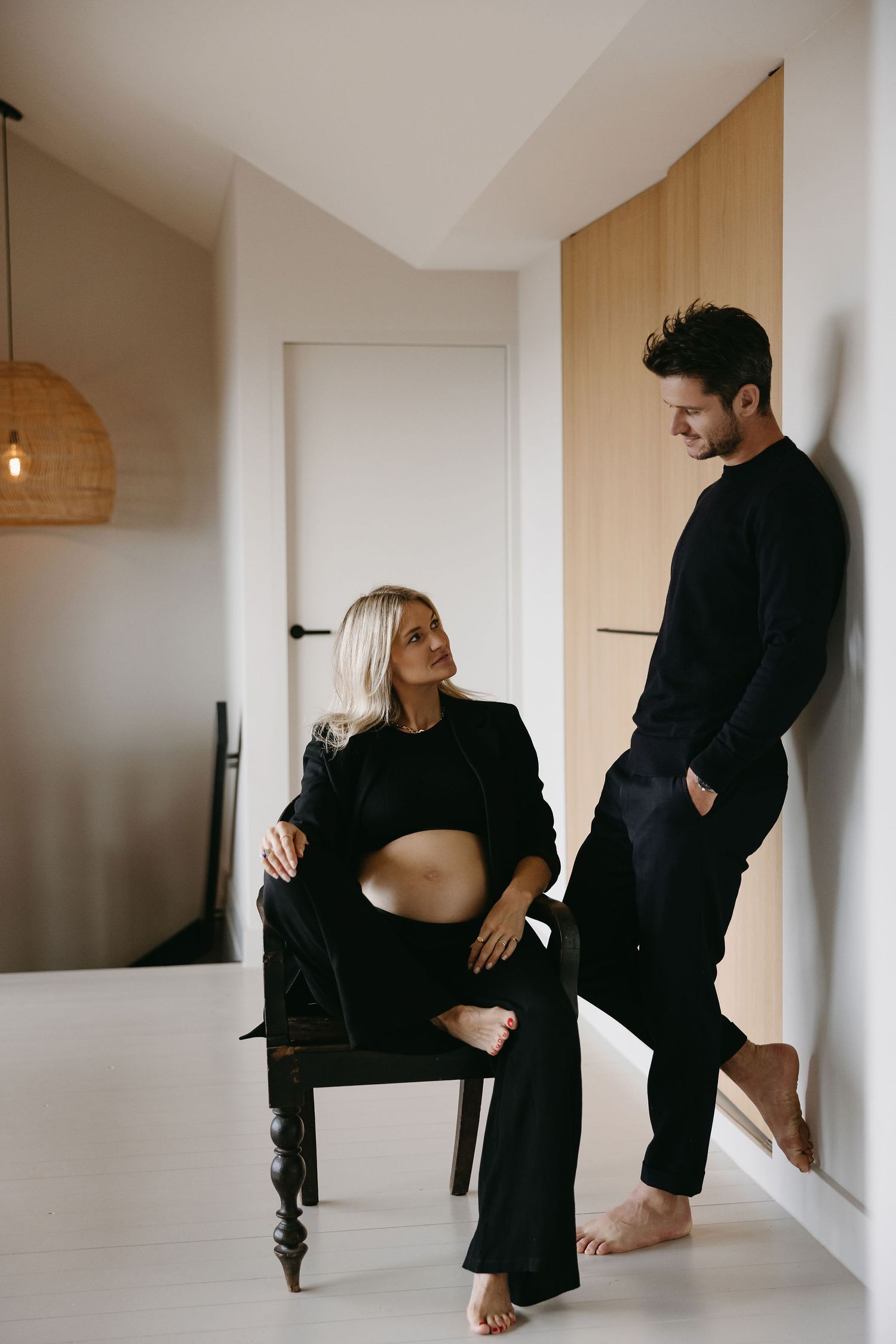 Indoor maternity photoshoot featuring couple in matching black outfits.