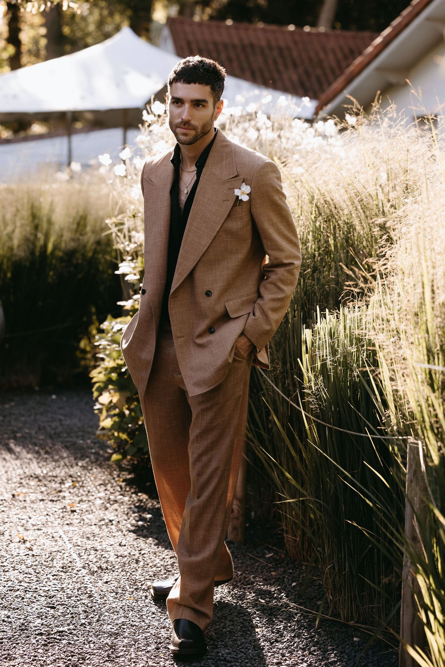Man in tan suit poses against backdrop of sunlit ornamental grasses.