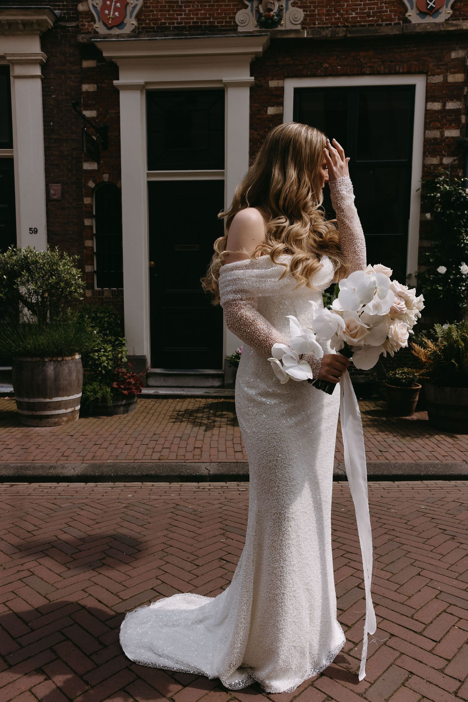 Couple in wedding attire embracing on brick courtyard.
