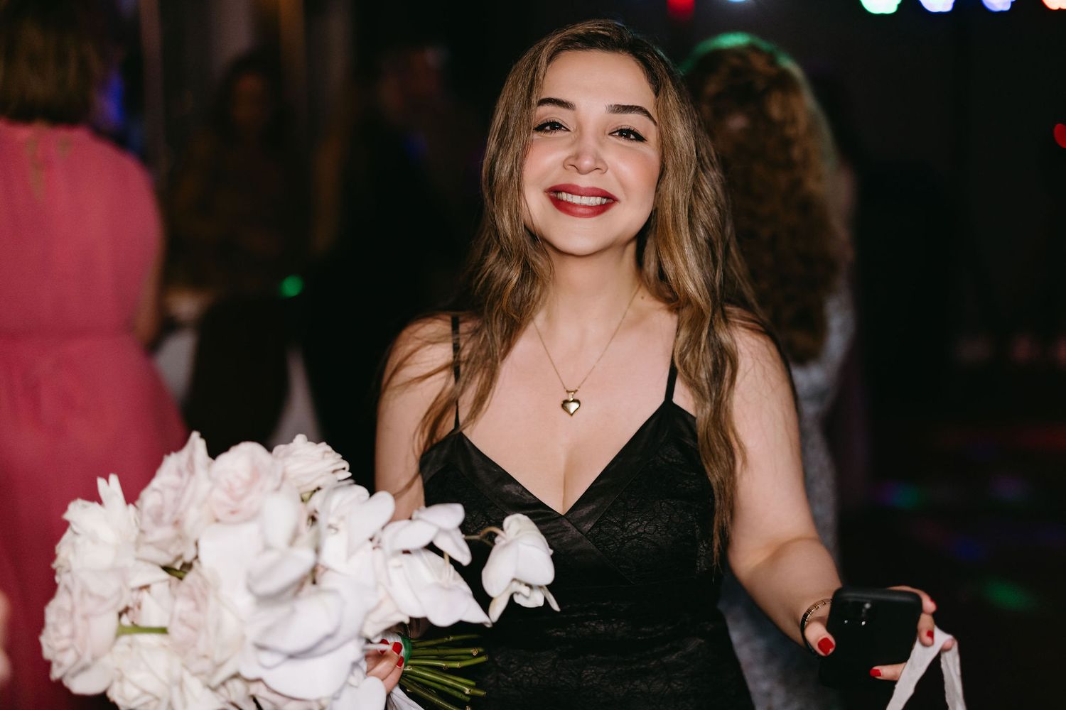 A woman in a black dress holding a white bouquet at an evening celebration.