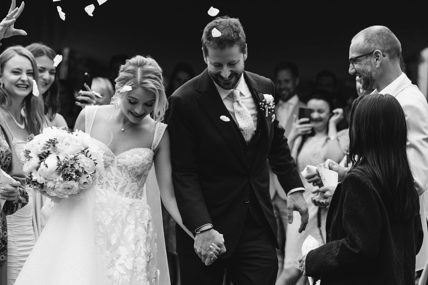 Black and white photo of joyful wedding recessional with flower petals being tossed.