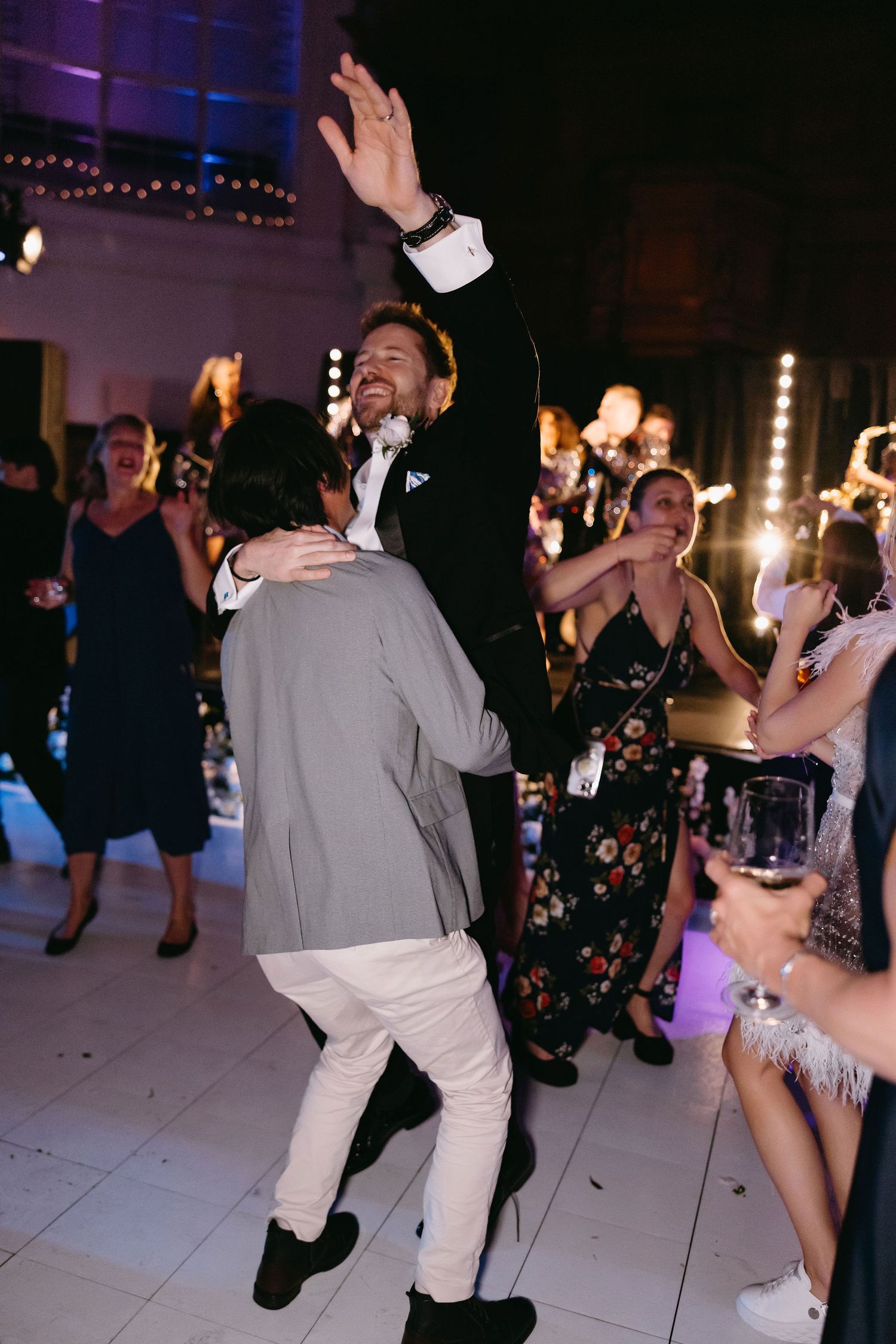 Wedding guests dancing energetically on a white dance floor with purple ambient lighting.