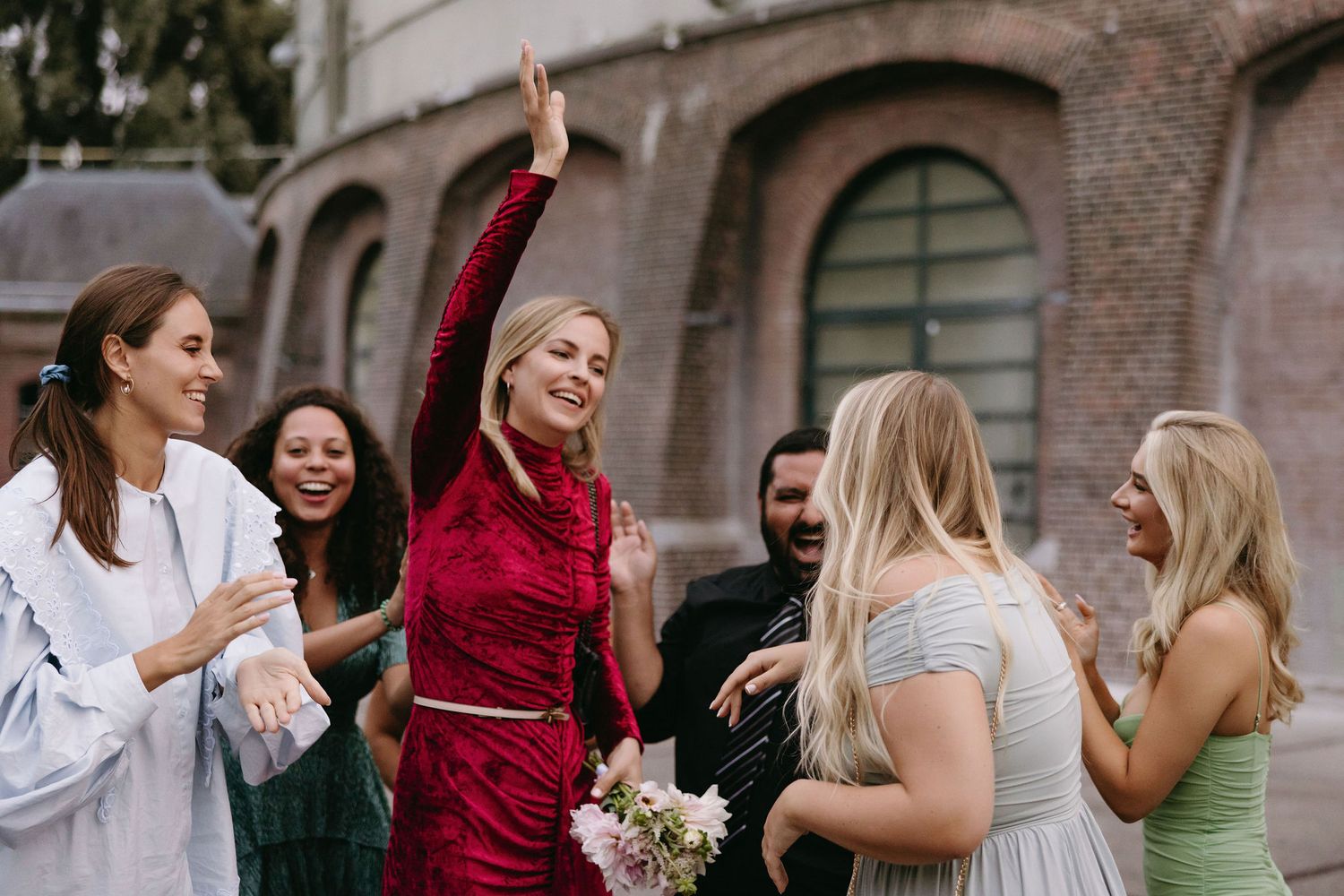 Wedding party celebrates outdoors with excited reactions and bouquet toss.