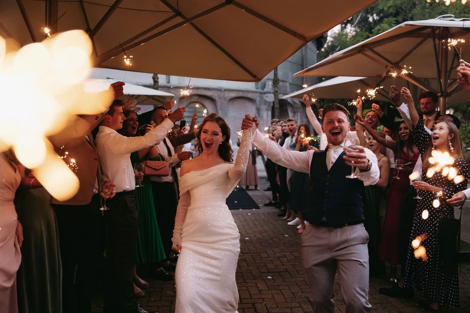 Wedding celebration under patio umbrellas with string lights at dusk.
