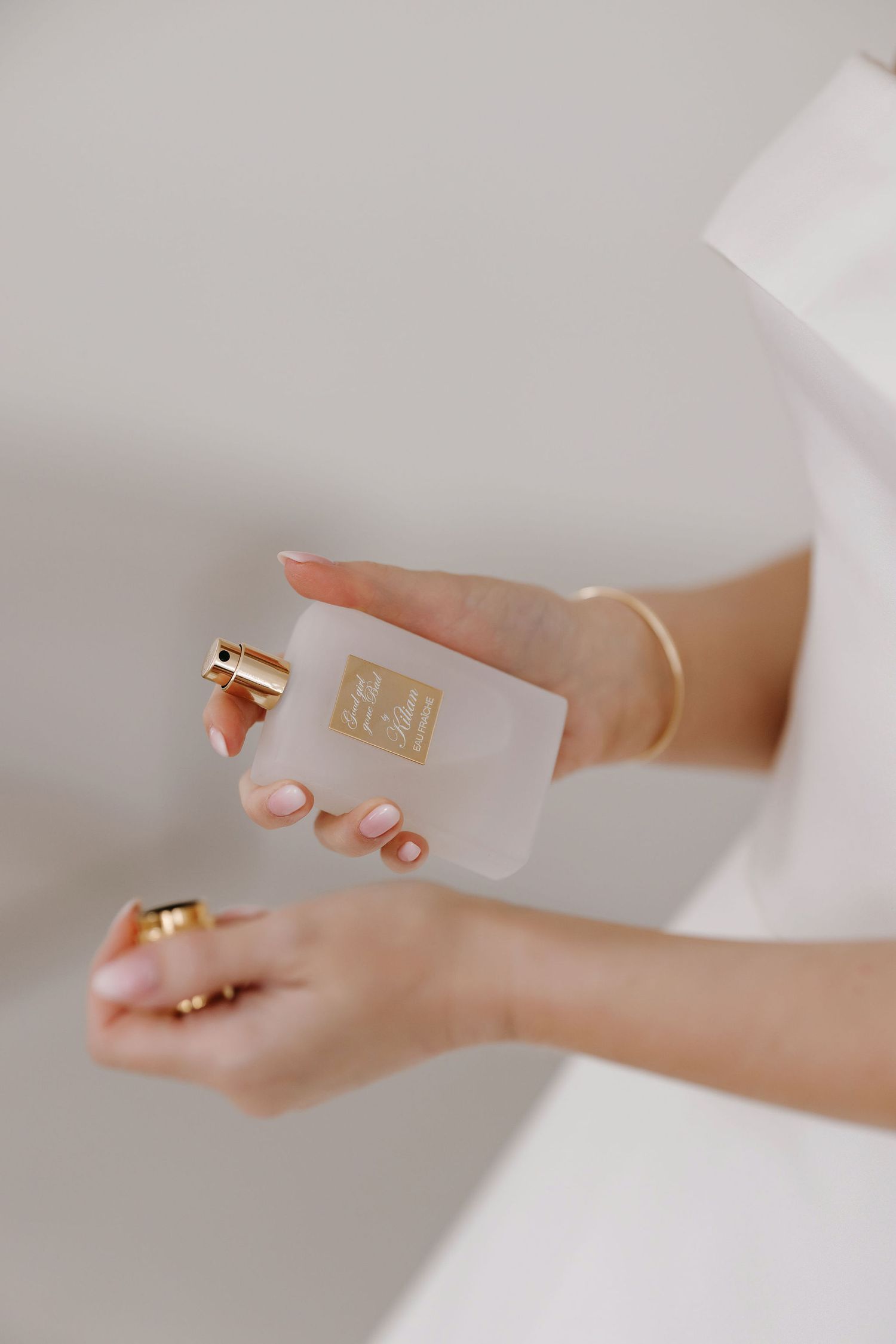 Delicate hands holding elegant white wedding rings against a soft neutral background.