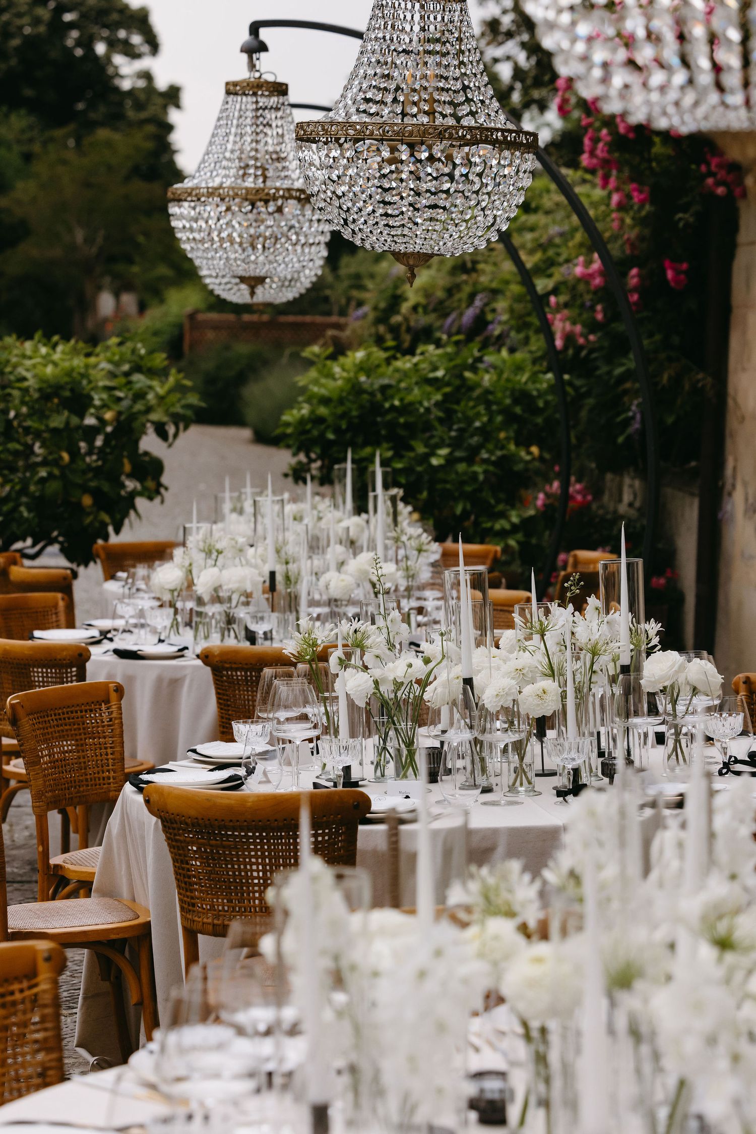 Elegant outdoor wedding reception table setup with crystal chandeliers and white floral arrangements.