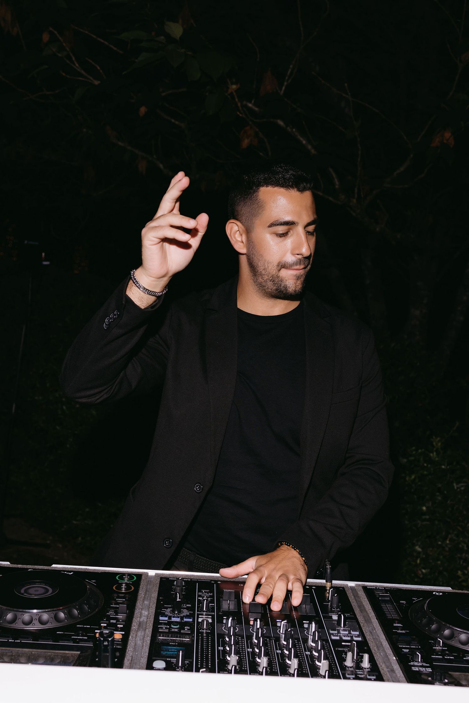 DJ performing at night with professional equipment wearing all black attire.