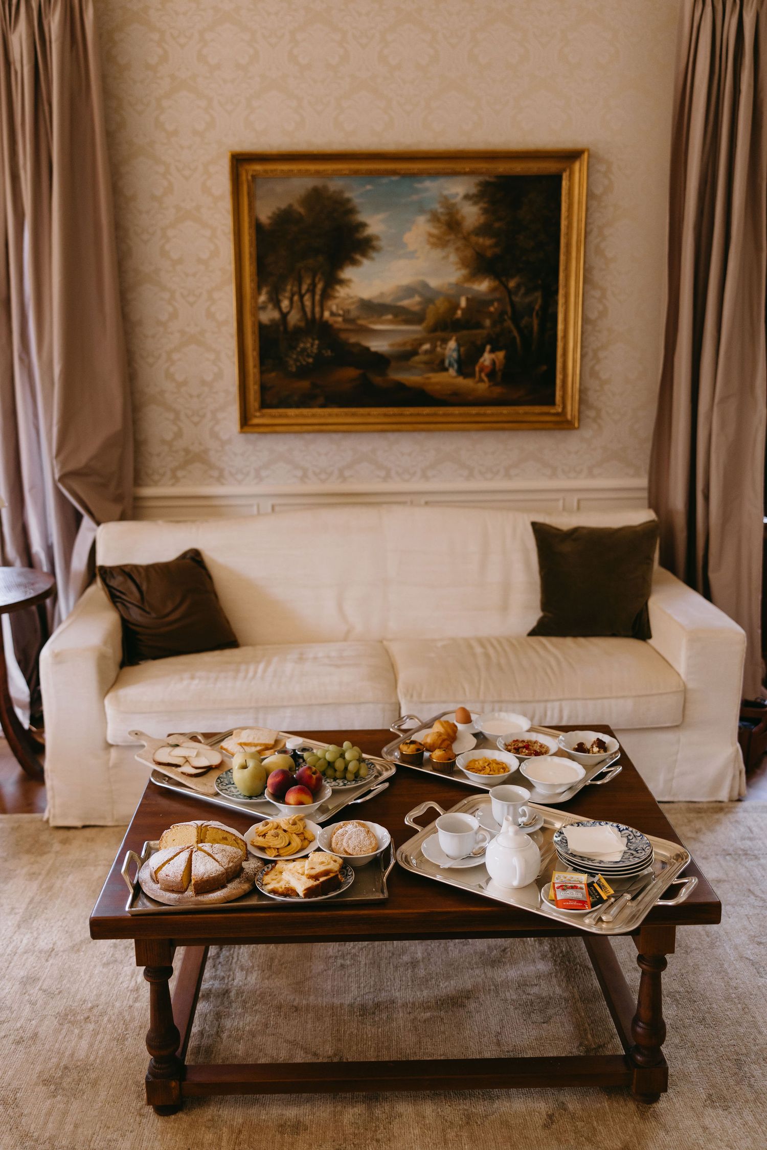 Elegant living room with landscape painting, white sofa, and breakfast spread on wooden coffee table.