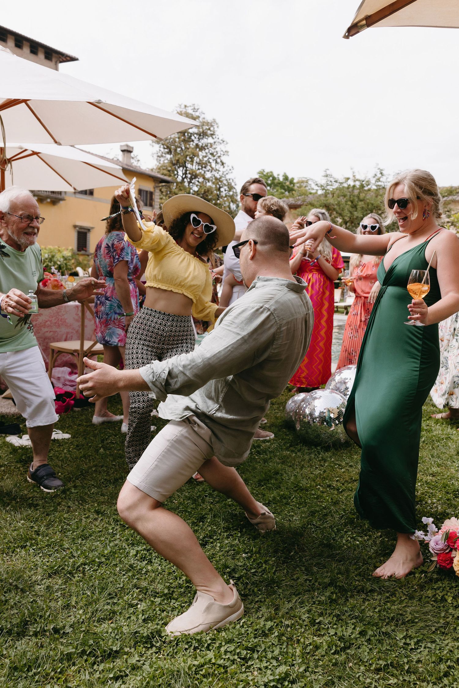 Wedding guests dancing and celebrating under patio umbrellas at an outdoor reception.