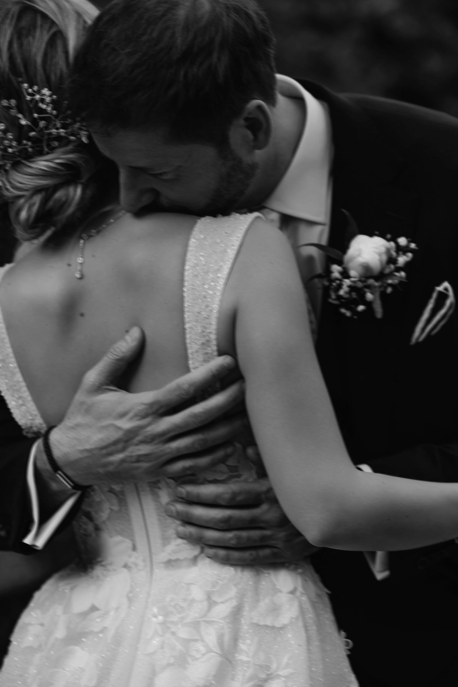 A tender black and white wedding moment showing a couple embracing, with the bride wearing a detailed lace gown.