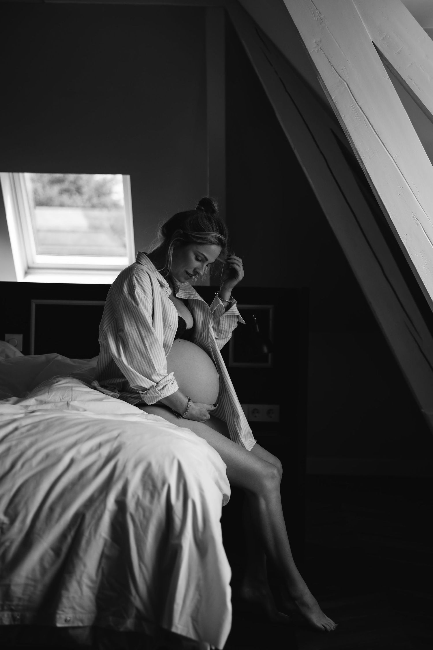 Black and white intimate maternity photo in attic bedroom with natural window light.