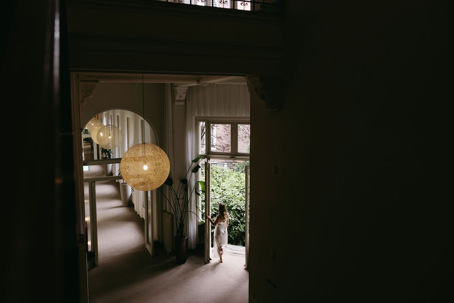 A distant view through doorways of someone in white standing in natural light.