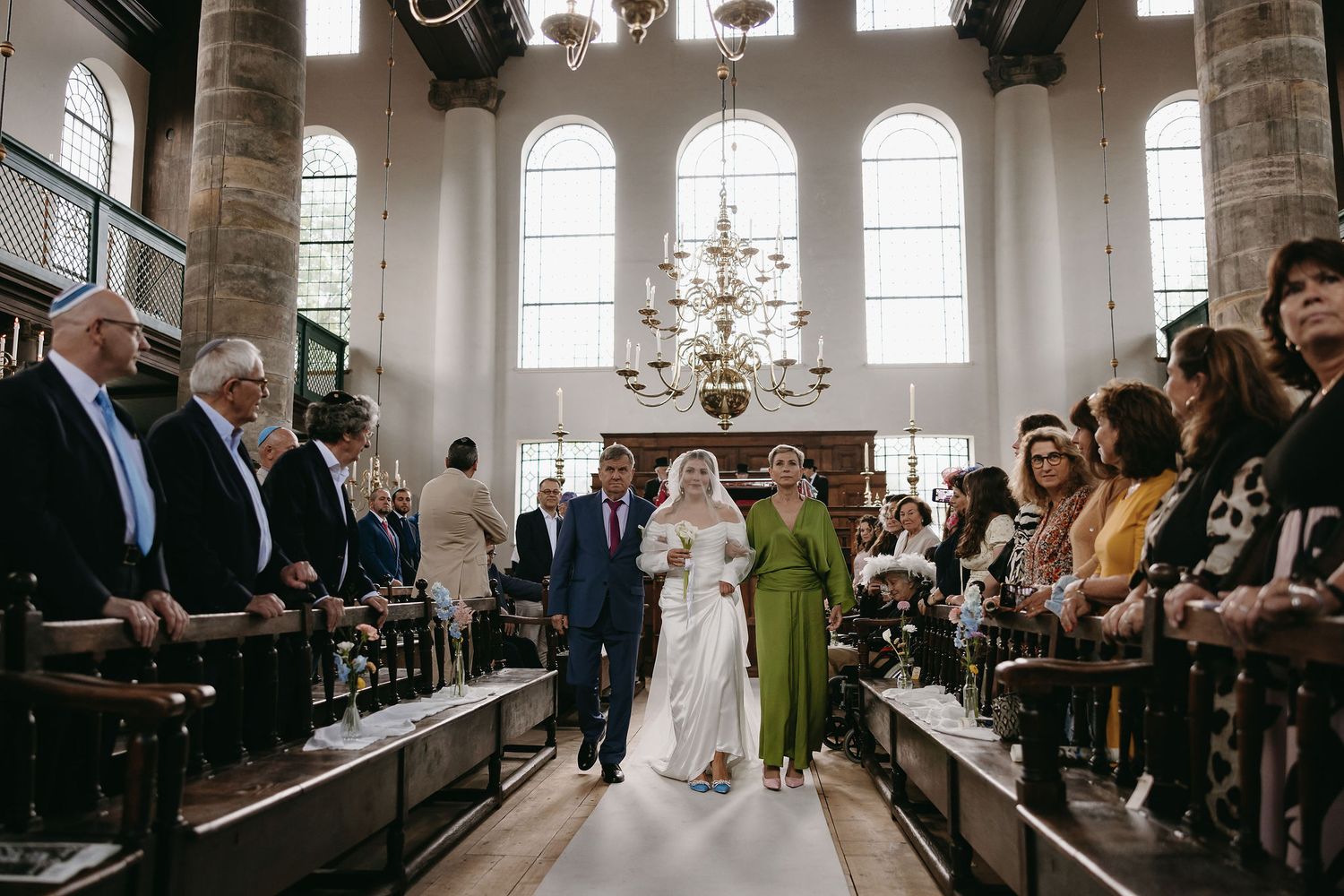Large historic chapel interior with arched windows and gathered wedding guests.