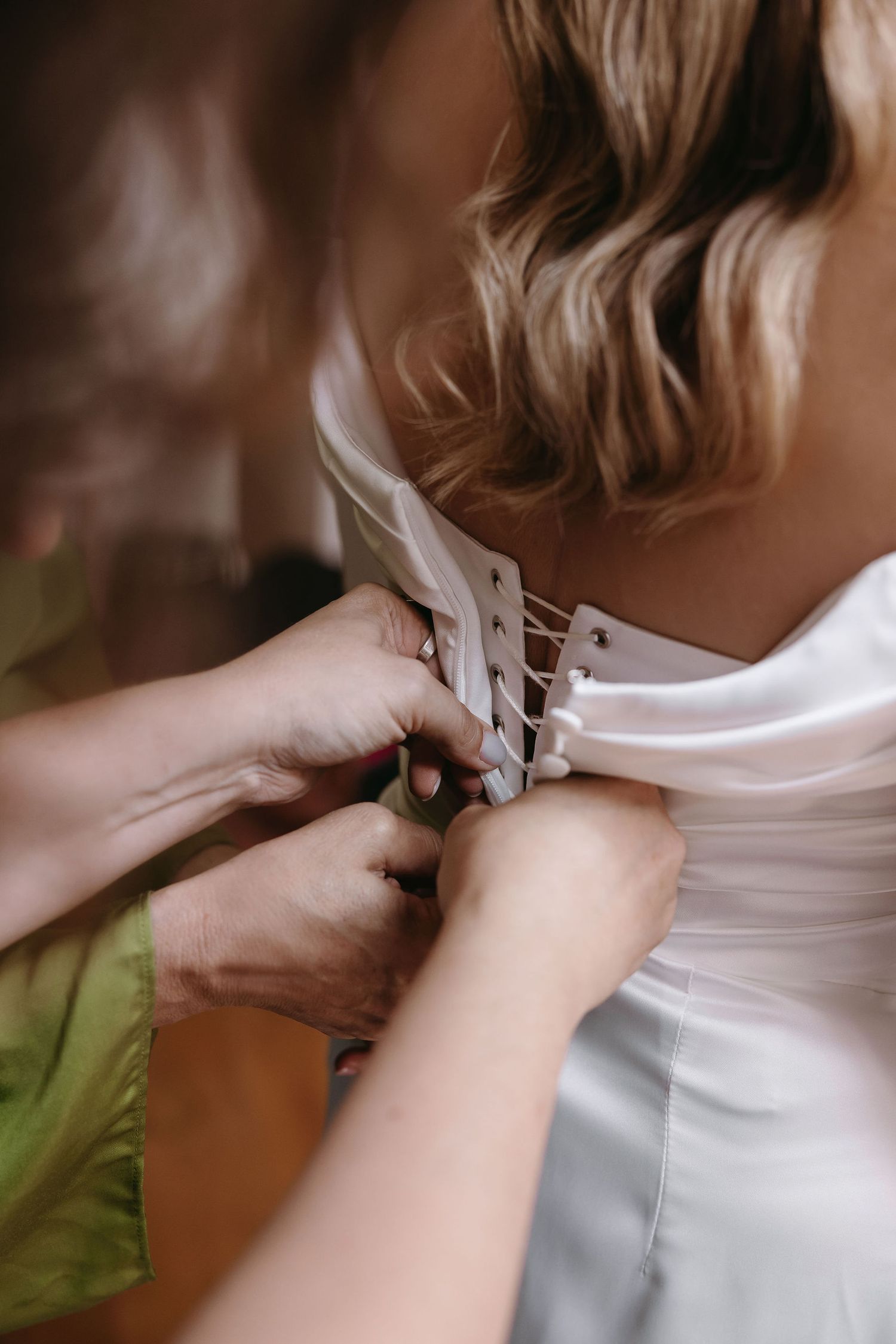 Close-up of hands fastening buttons on back of white wedding dress.