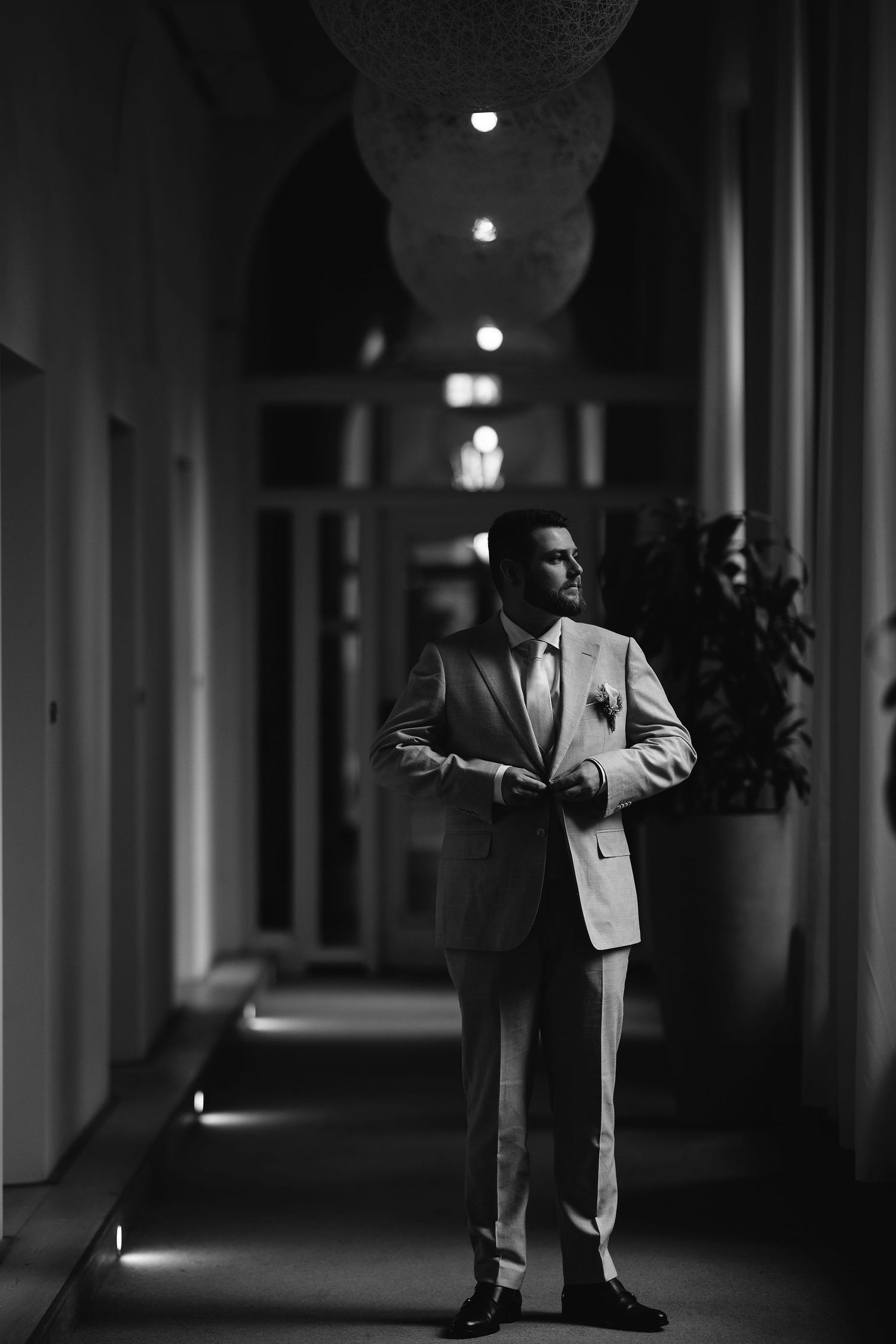 Dramatic black and white portrait in dimly lit hallway with architectural columns.