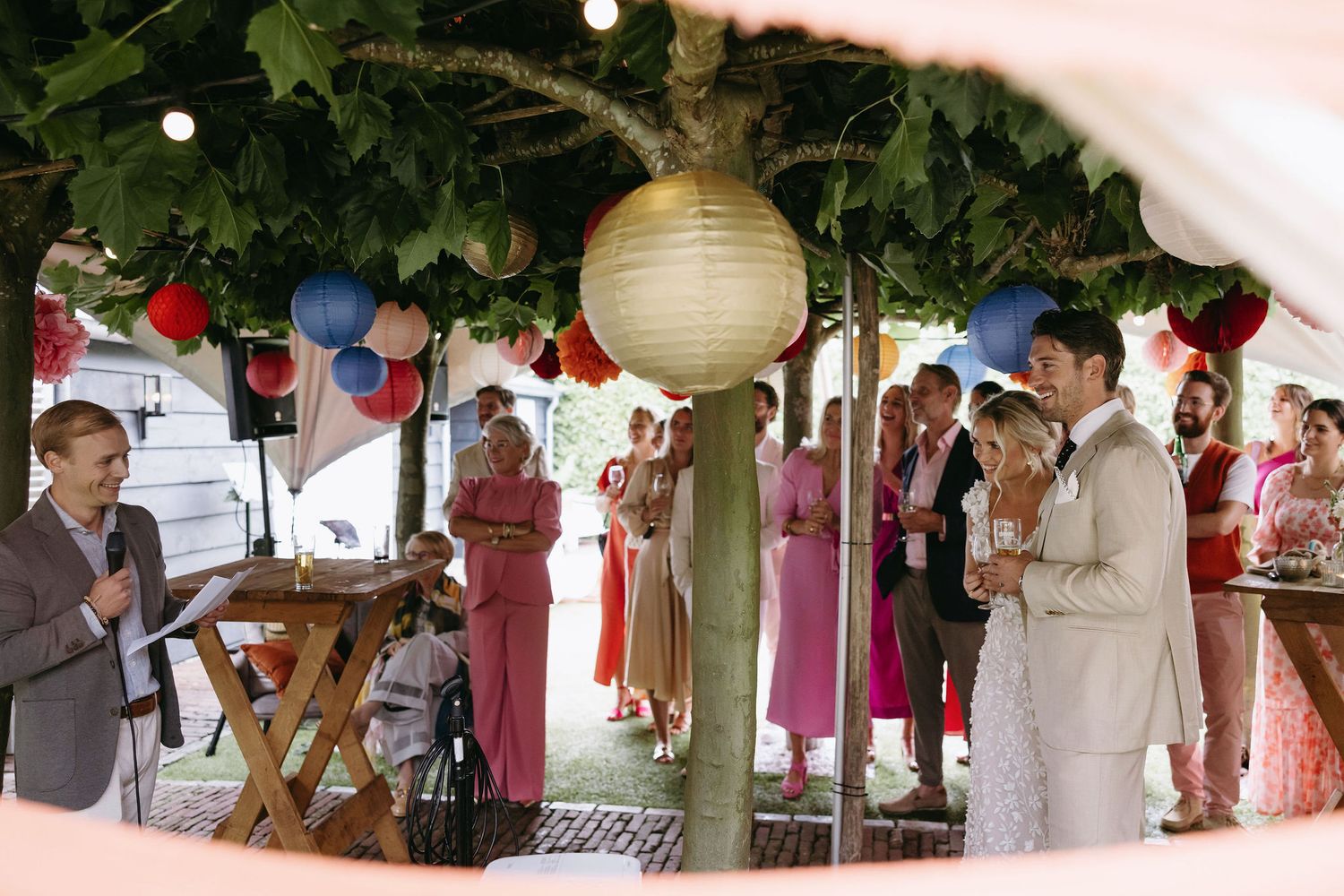 Outdoor wedding reception with paper lanterns and greenery decorations.