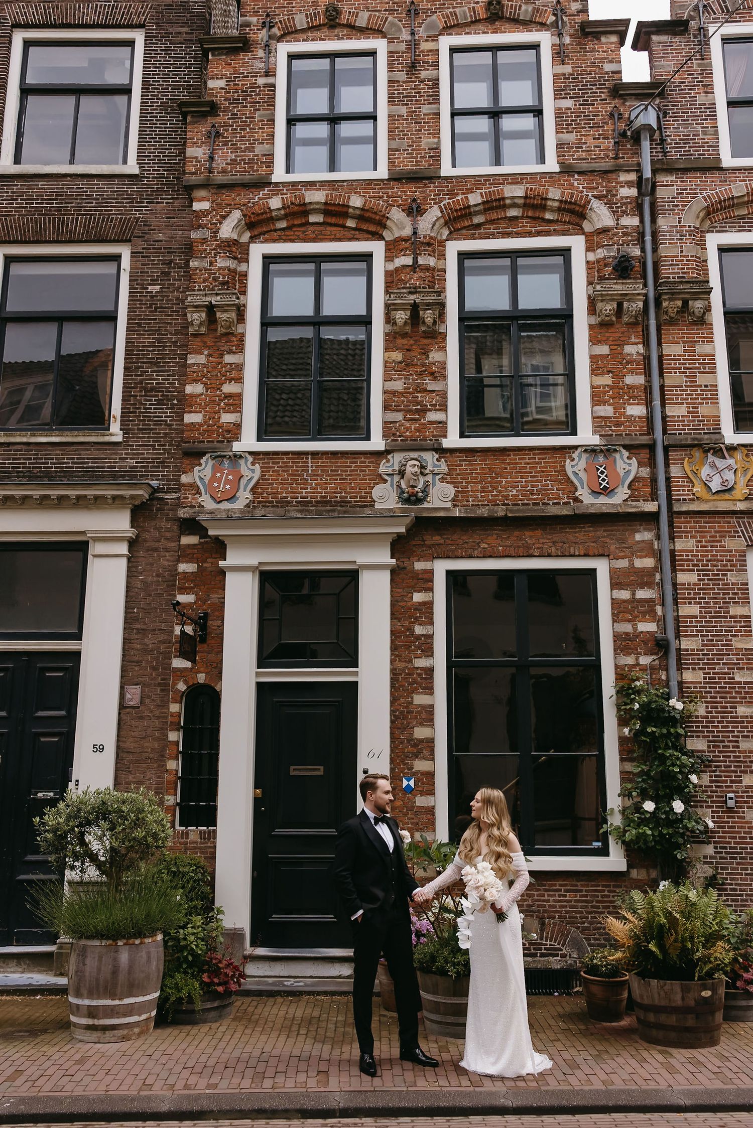 Couple in wedding attire posing in front of traditional Dutch brick buildings and cobblestone streets.