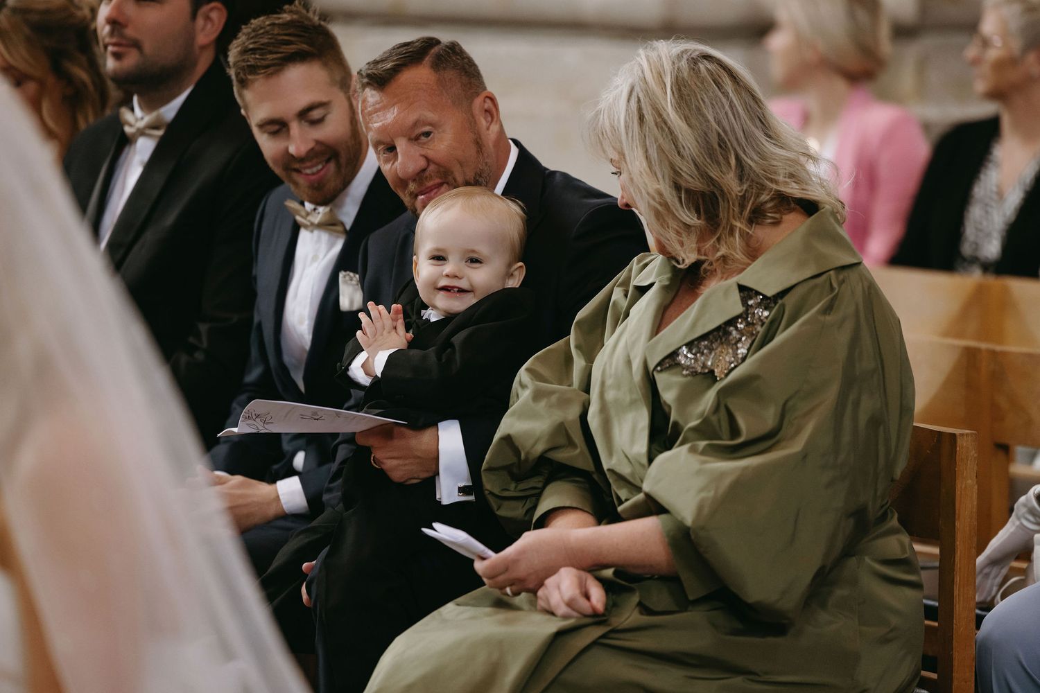 Wedding ceremony attendees seated in church pews sharing joyful moments together.