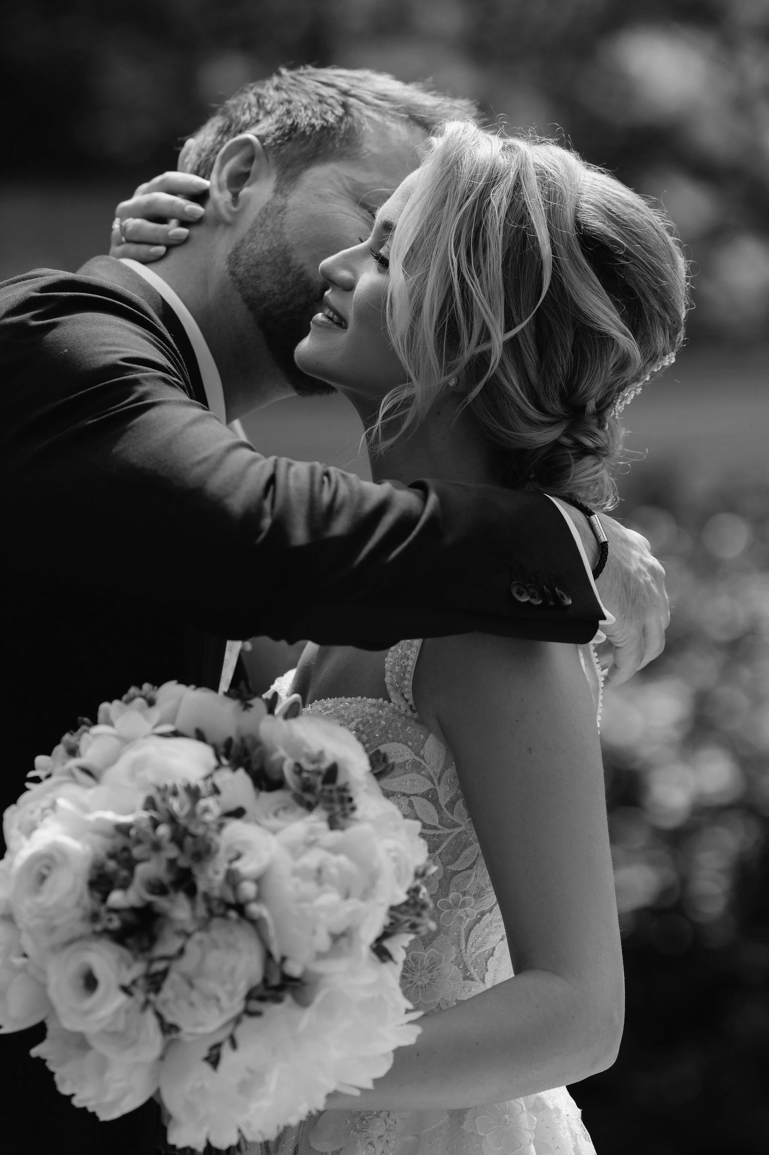 Black and white outdoor portrait with white floral bouquet and romantic embrace.