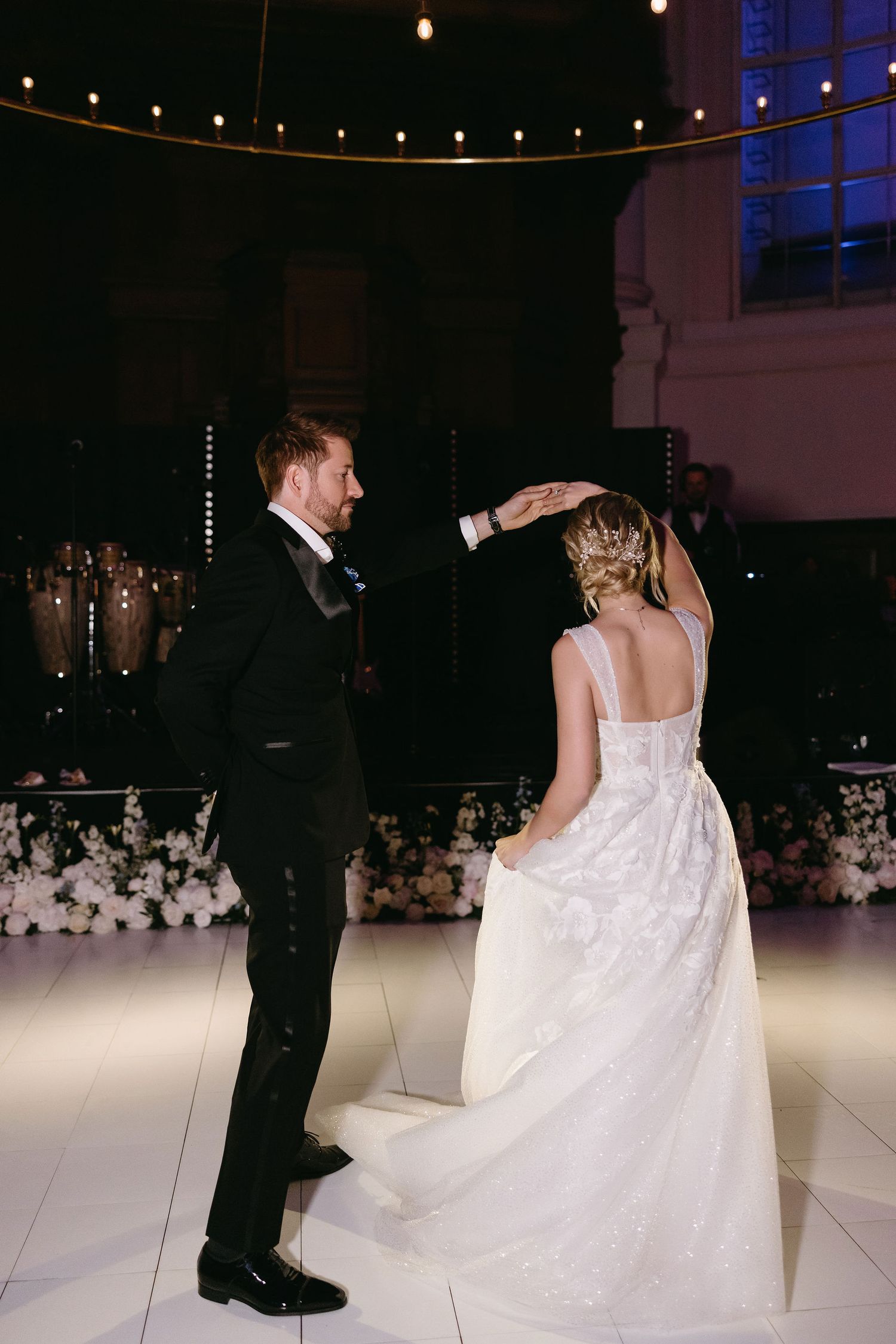 Romantic first dance moment on an illuminated white dance floor with string lights overhead.