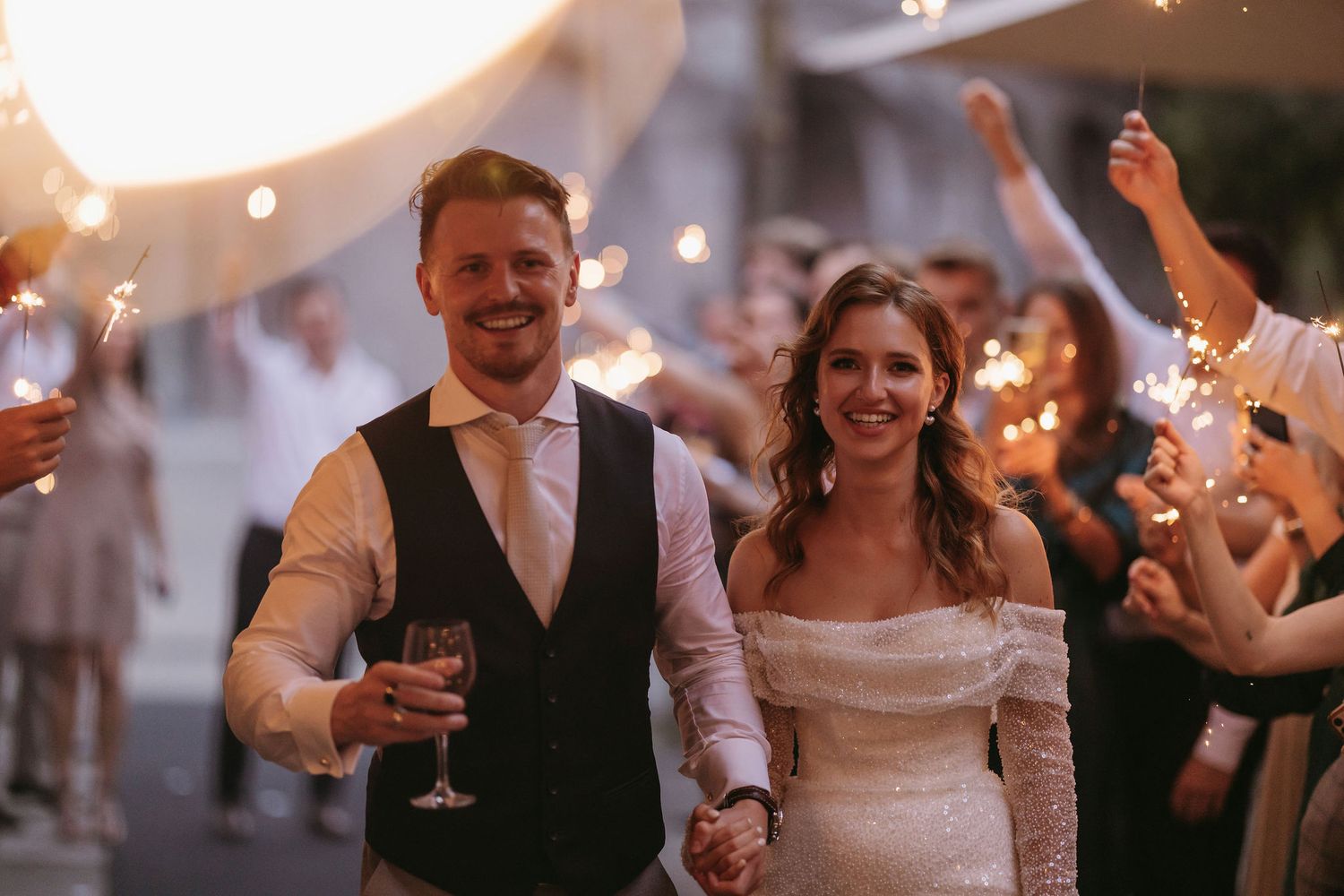 Wedding celebration with string lights and guests raising champagne glasses.
