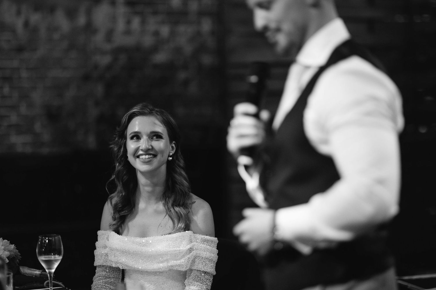 Black and white photo of a wedding reception speech moment in a dimly lit venue.