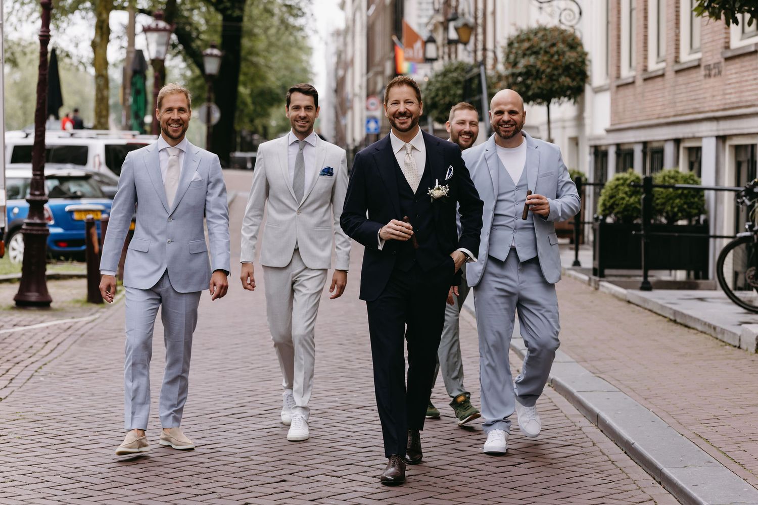 Groomsmen walking together in light and dark suits on a city street.