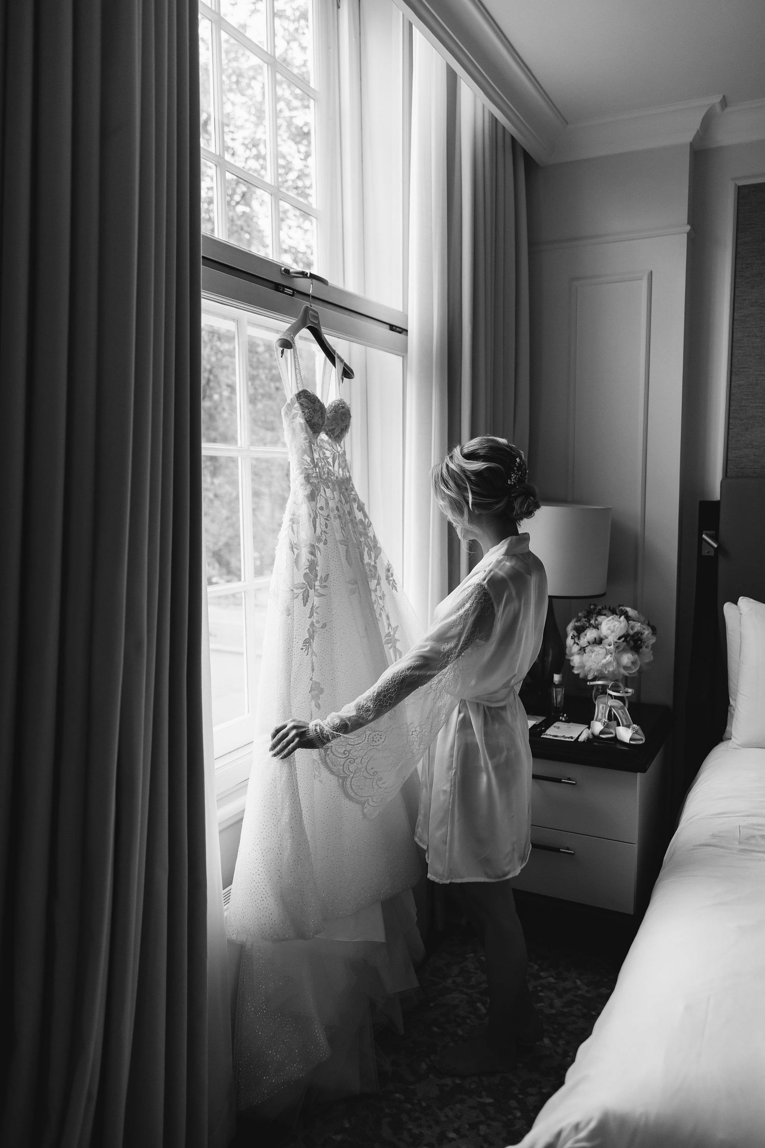 Black and white shots of a wedding dress hanging by windows in an elegant room.