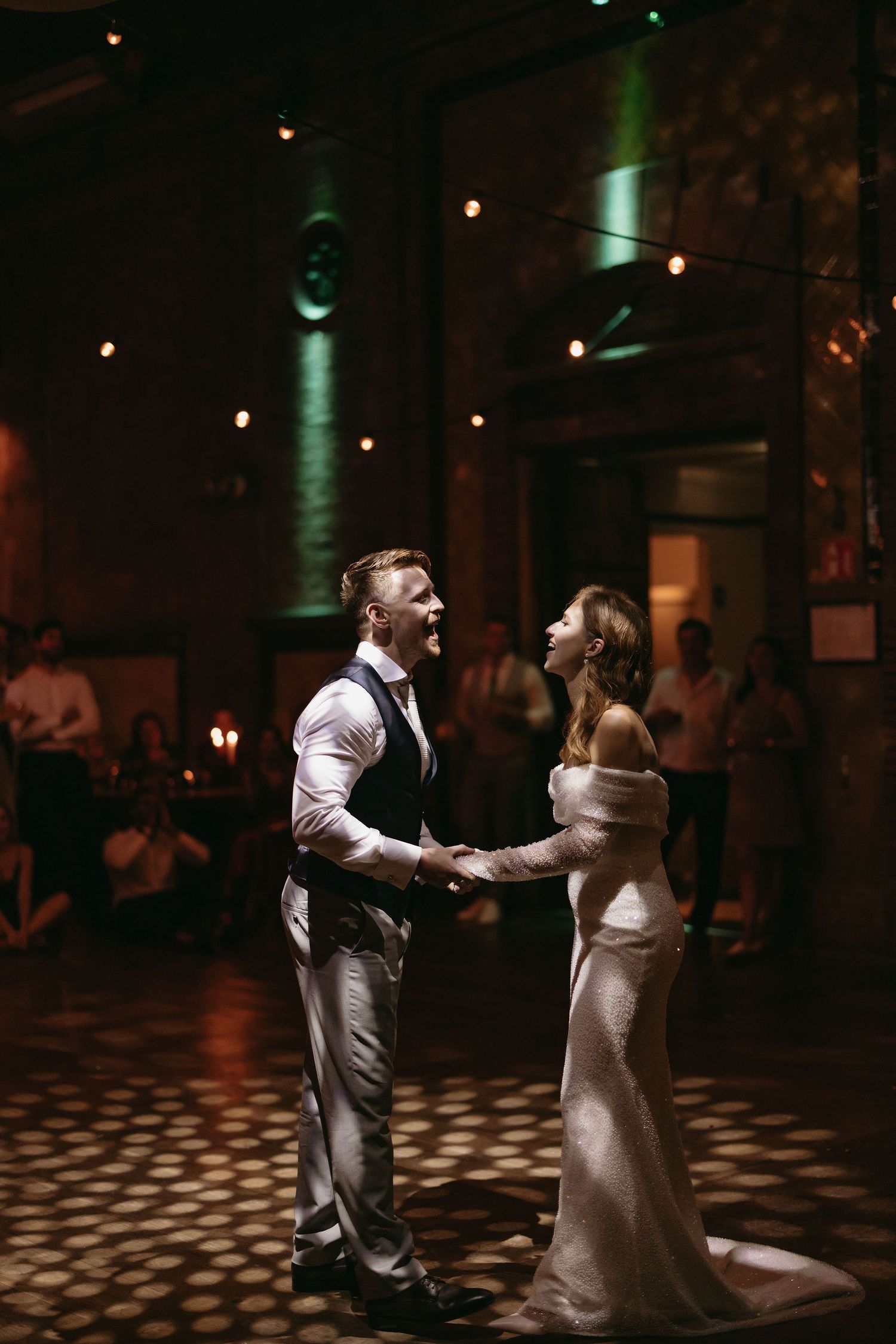 Newlyweds dancing together under dramatic lighting with spotlit patterns on the floor.