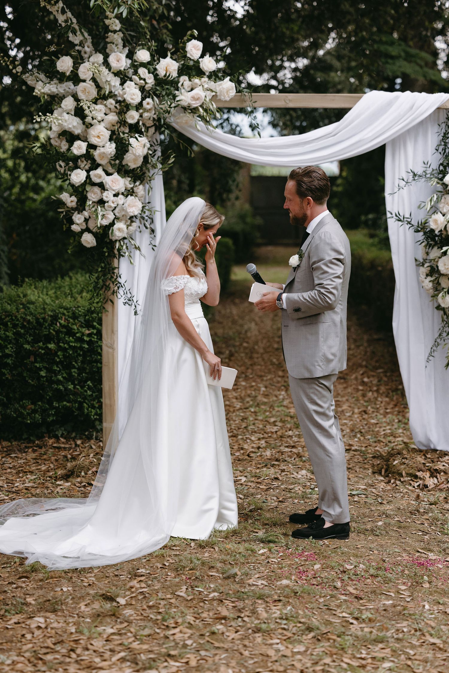 Wedding arch decorated with white roses and flowing fabric in a garden setting.