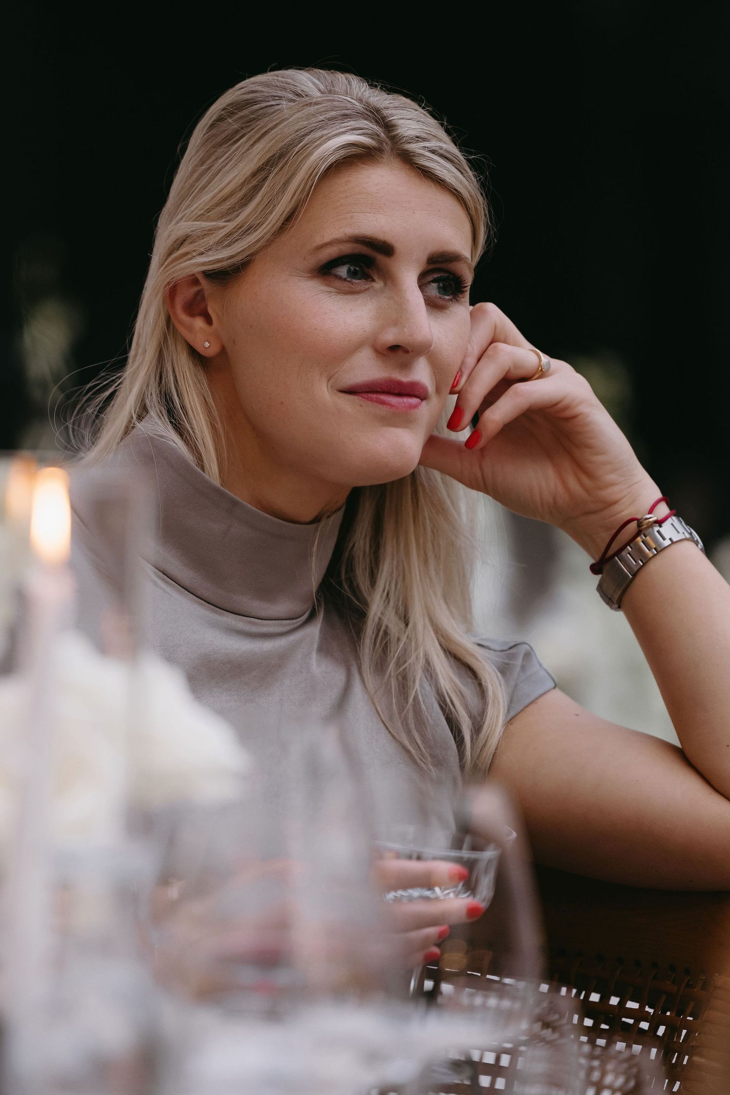 Woman in beige turtleneck sits contemplatively at an elegant dinner setting.