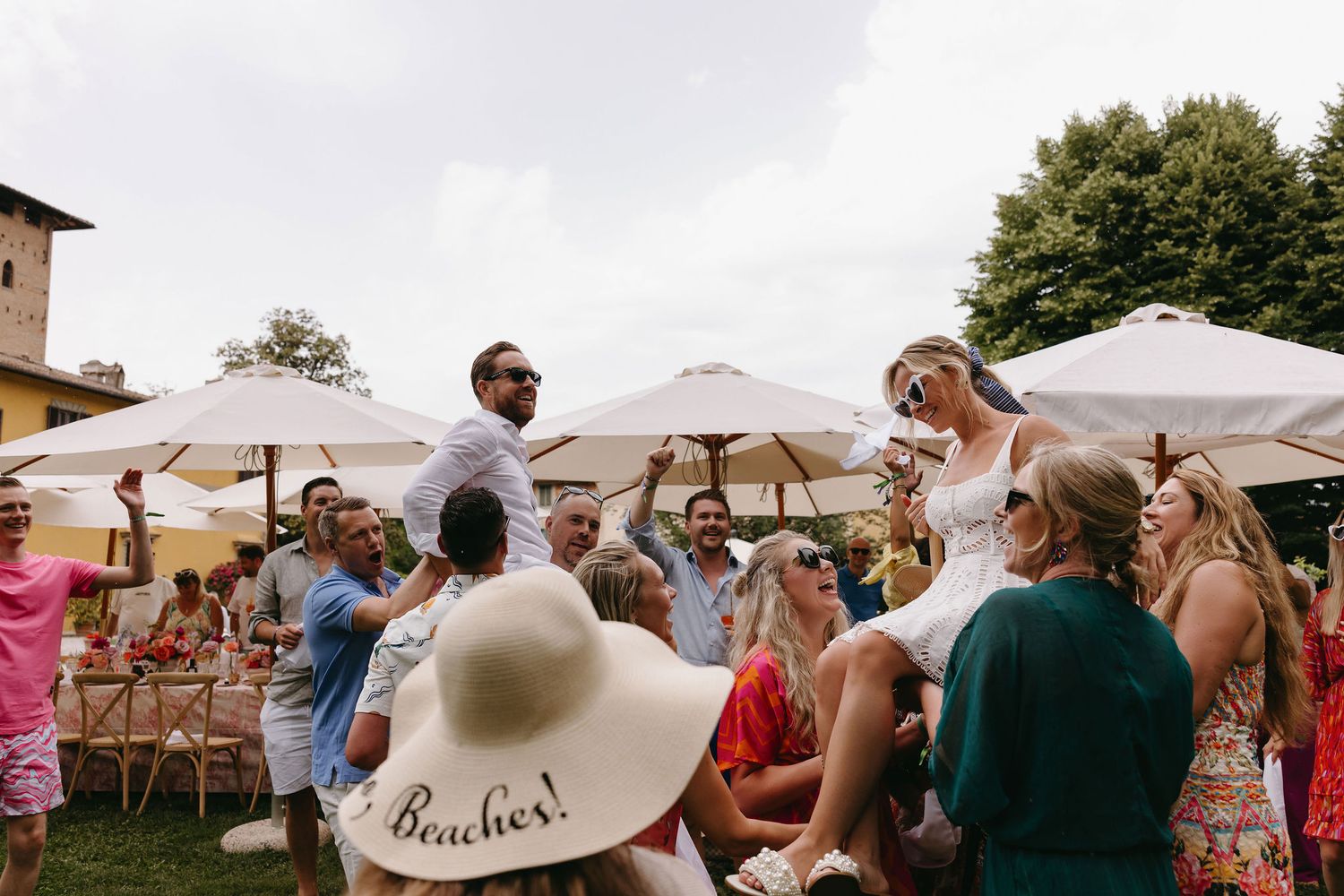 Outdoor wedding reception with white umbrellas and guests gathered under a bright summer sky.