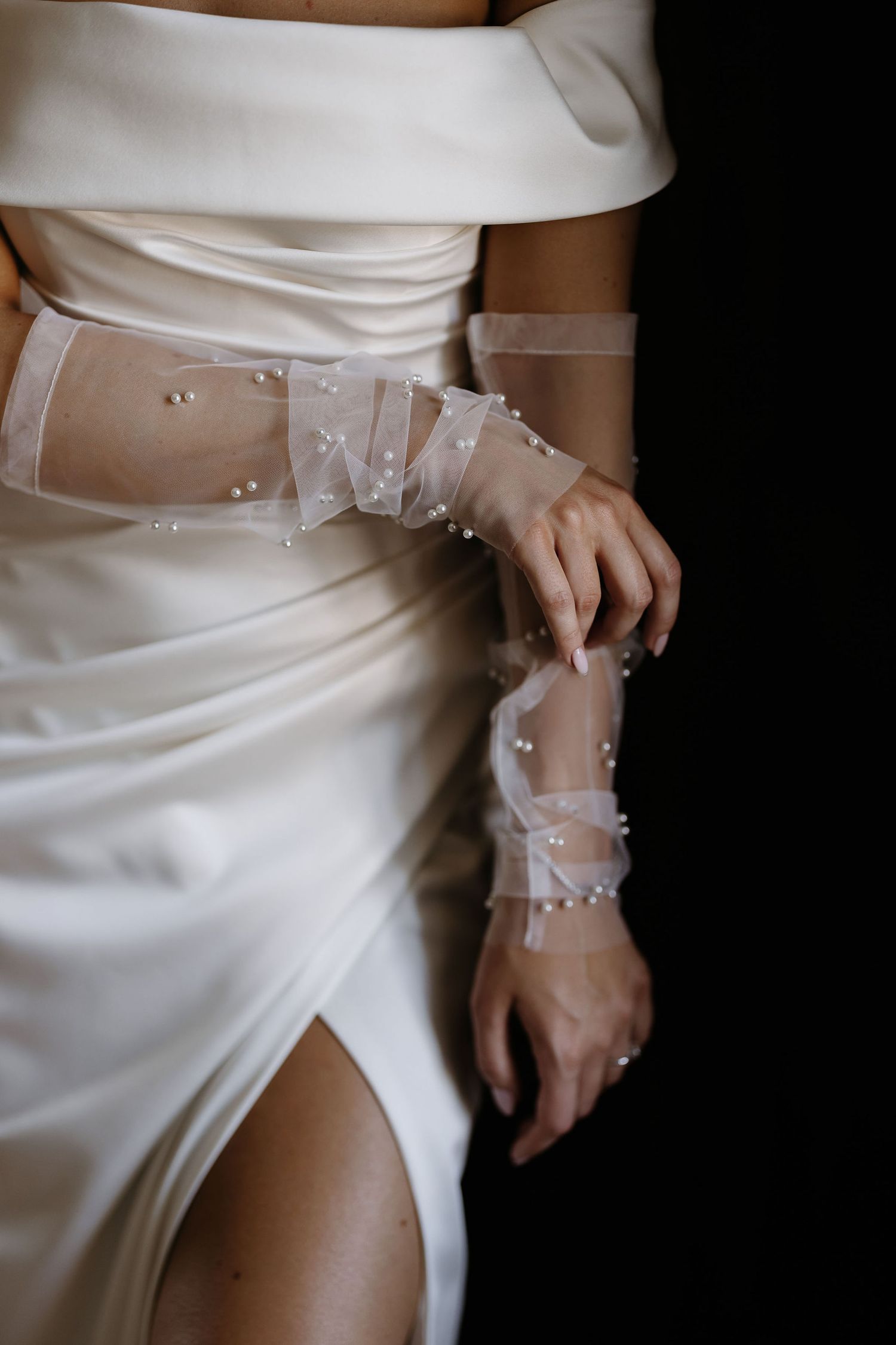Delicate white lace detailing adorns the wrist of a person wearing an elegant white wedding gown.