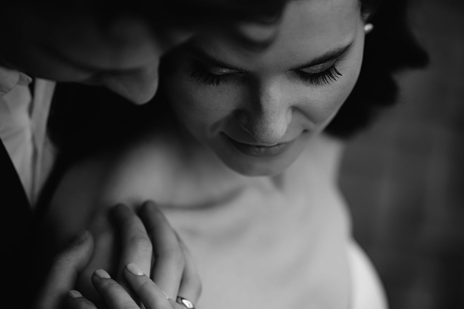 A close-up artistic black and white photograph showing hands with a wedding ring.