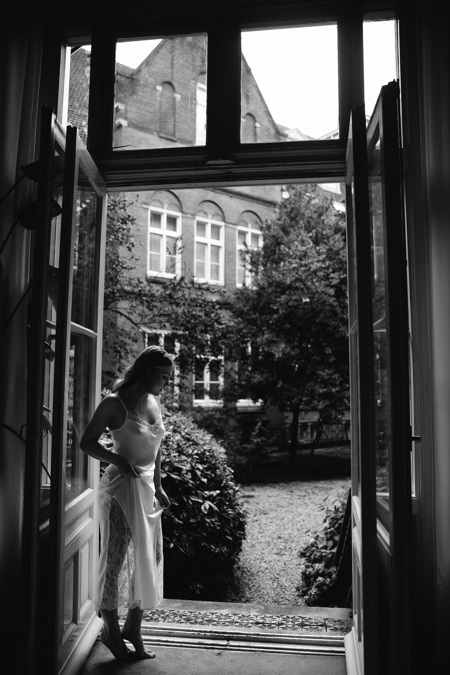 A silhouetted figure stands in a doorway overlooking a courtyard with historic architecture in black and white.