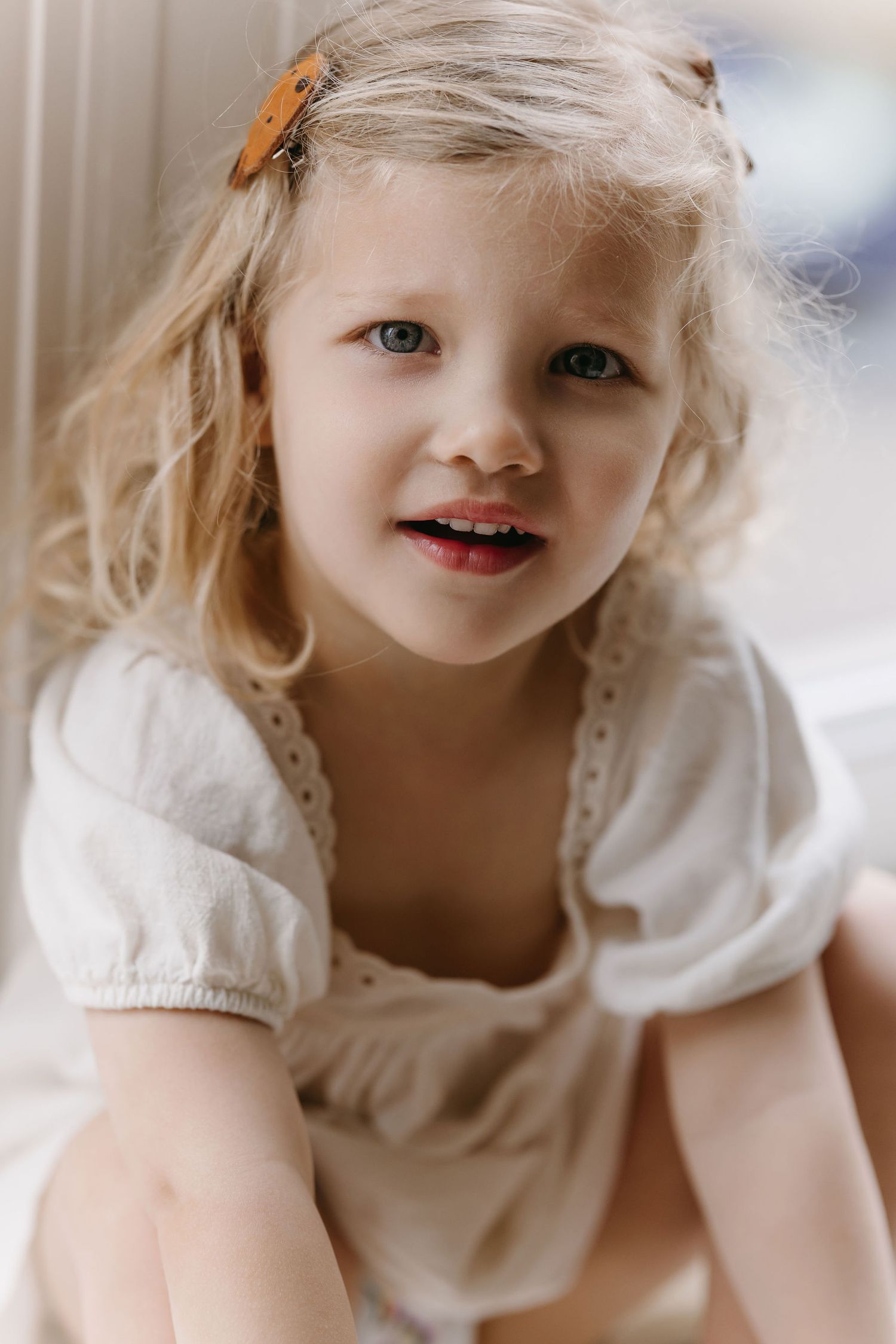 Young child in white dress with blonde hair and orange hair clip.