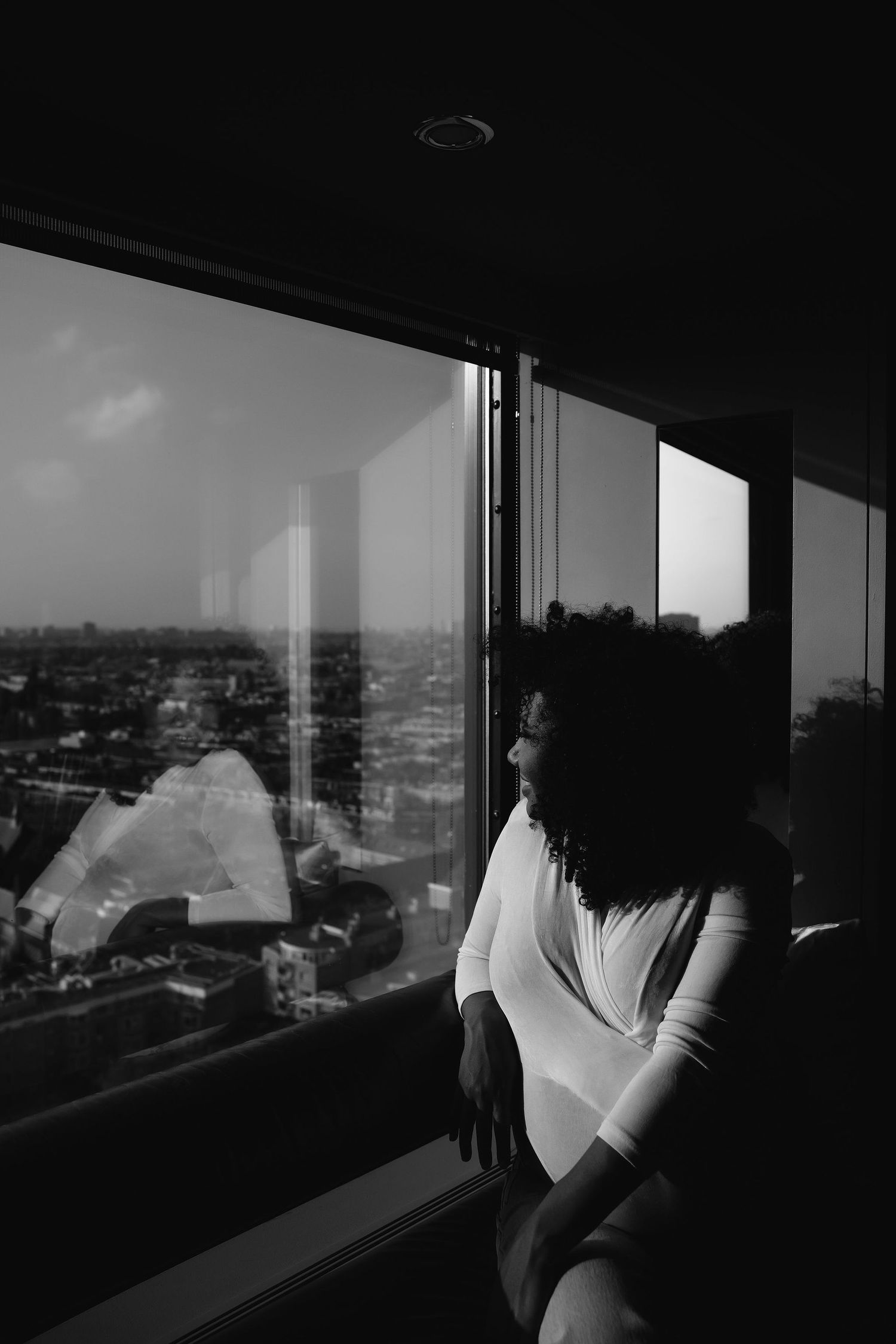 Dramatic black and white portrait by window overlooking city skyline.
