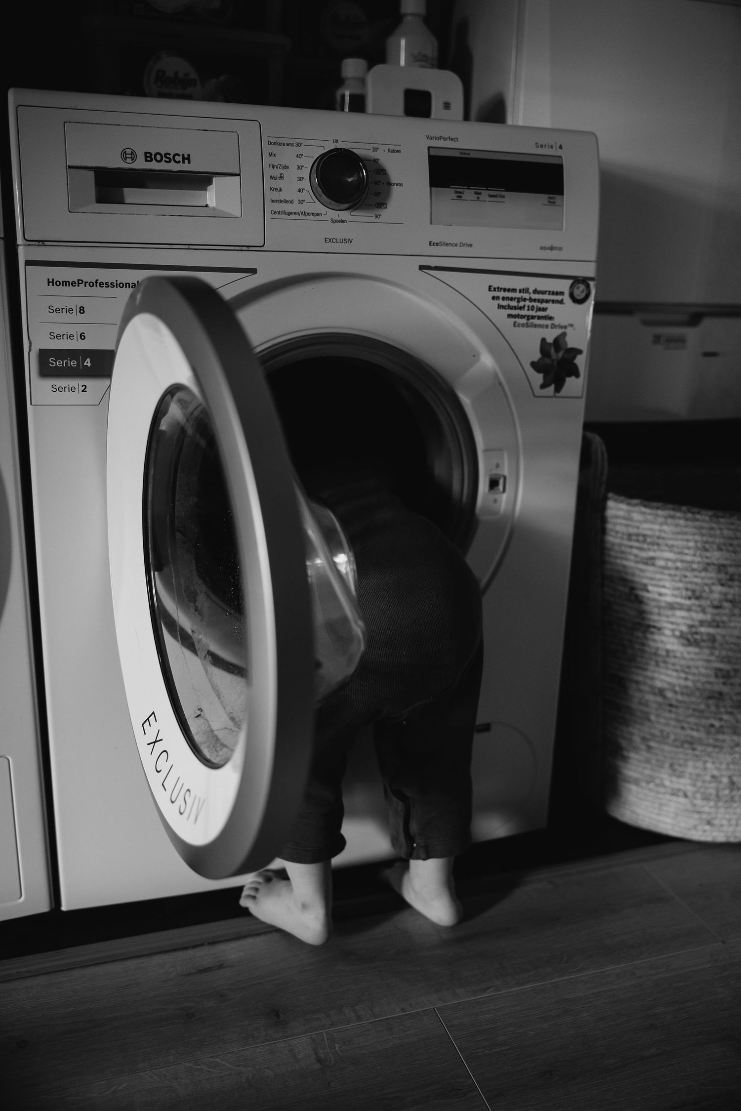 Black and white image of small feet visible through an open washing machine door.