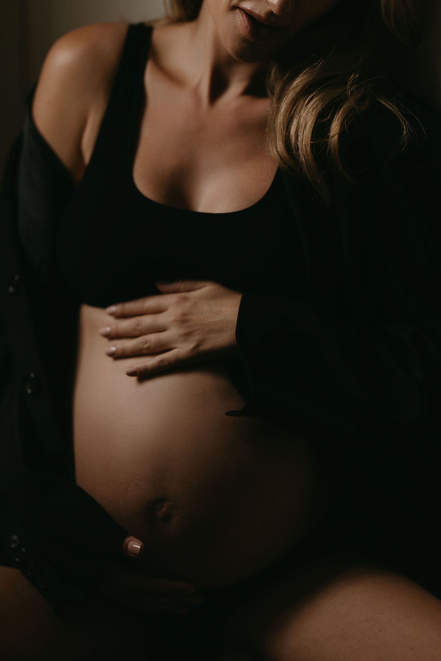 Moody silhouette maternity photo showing pregnant belly in dark lighting.