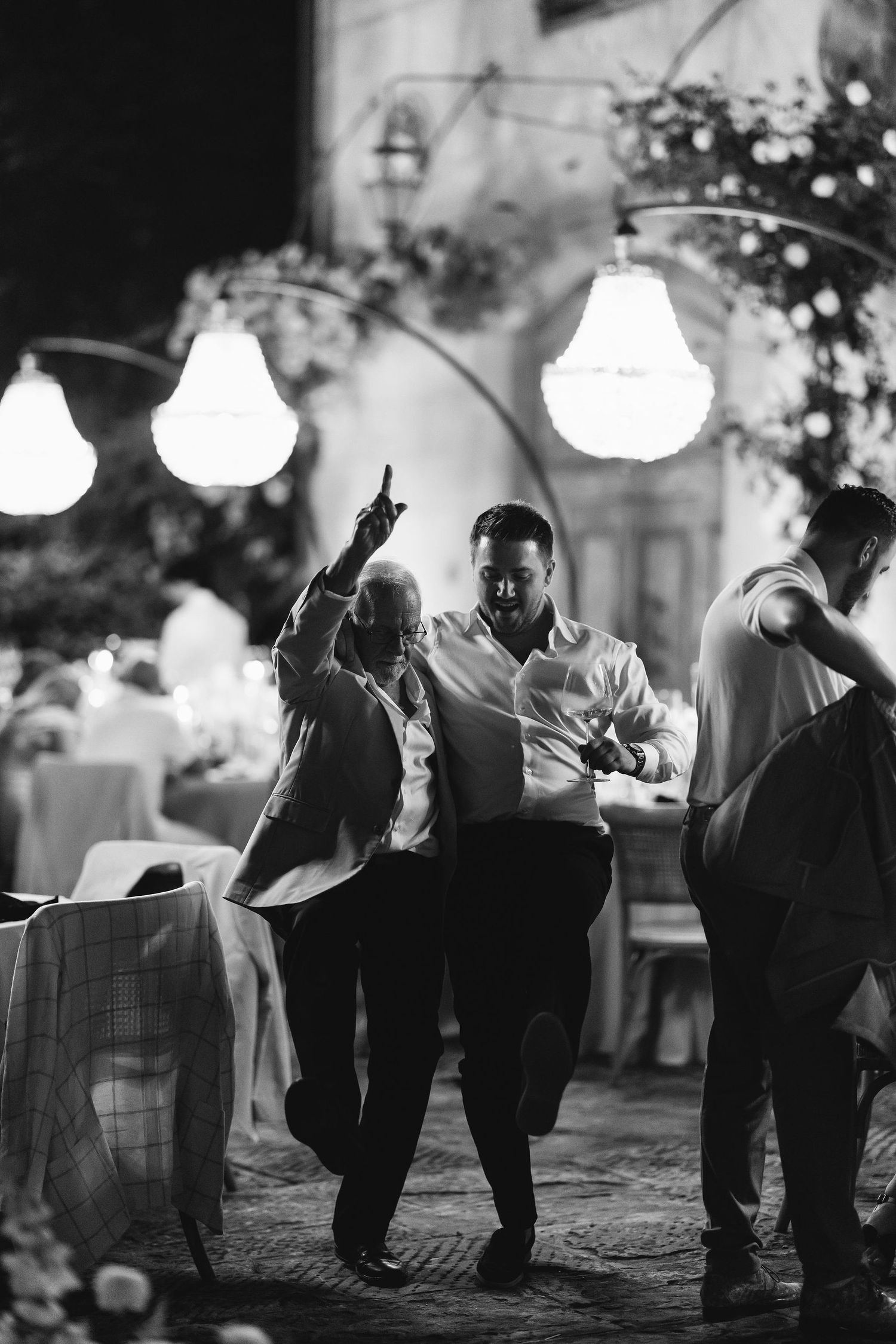 People dancing and celebrating at a nighttime wedding reception under glowing lanterns.