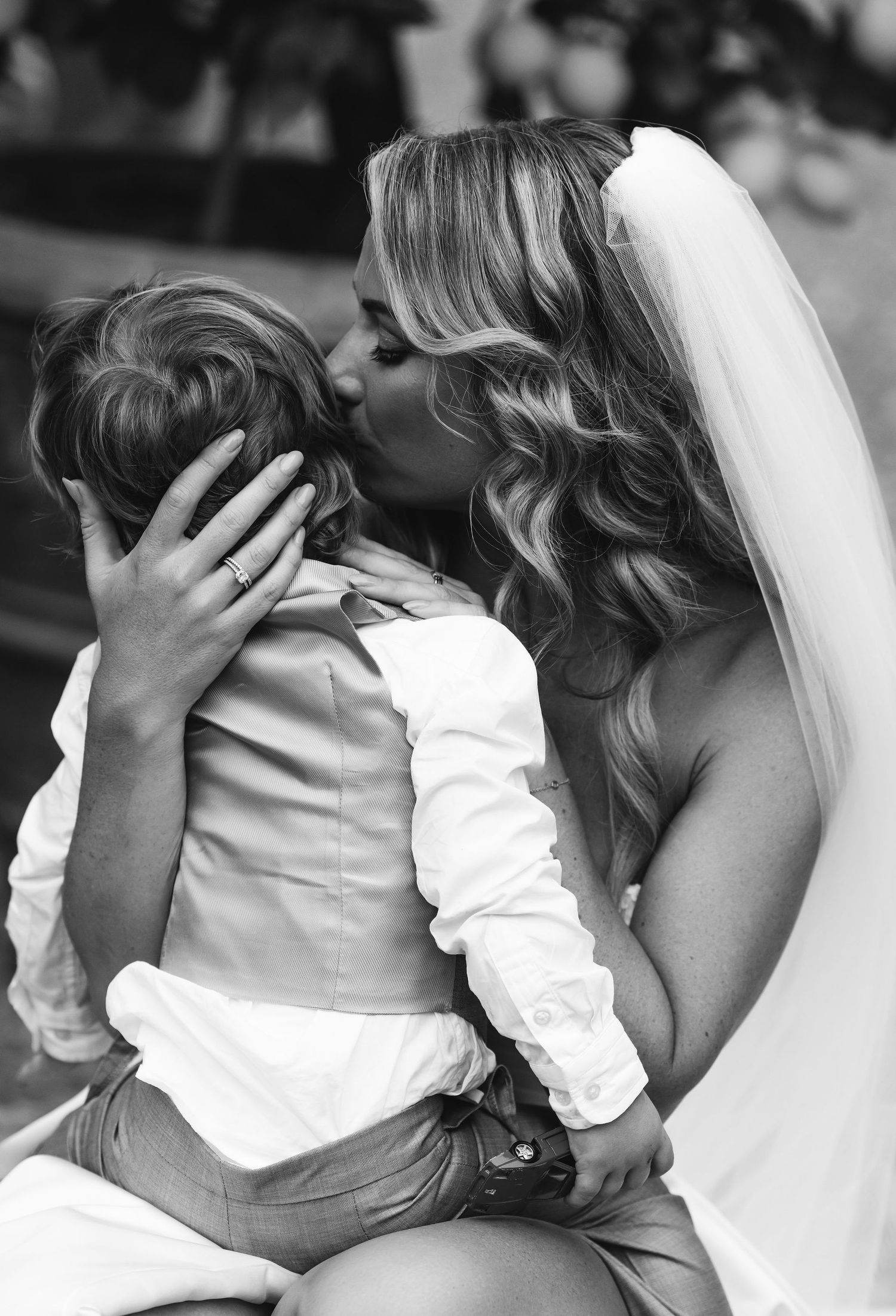 Tender black and white moment between a bride in white dress and young ring bearer.