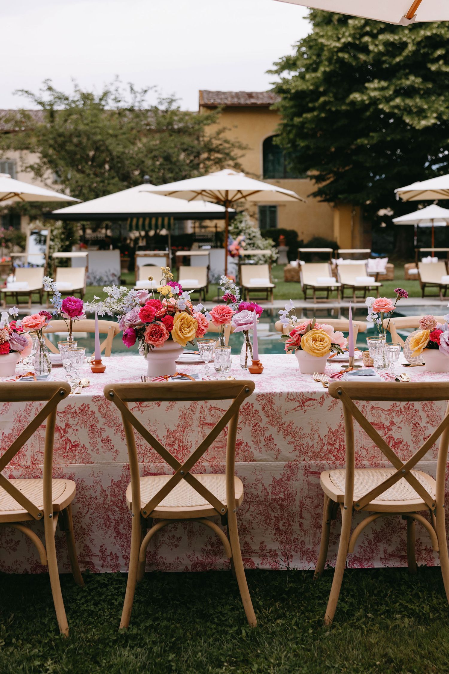 An elegant outdoor wedding reception table with pink floral centerpieces and crossback chairs.